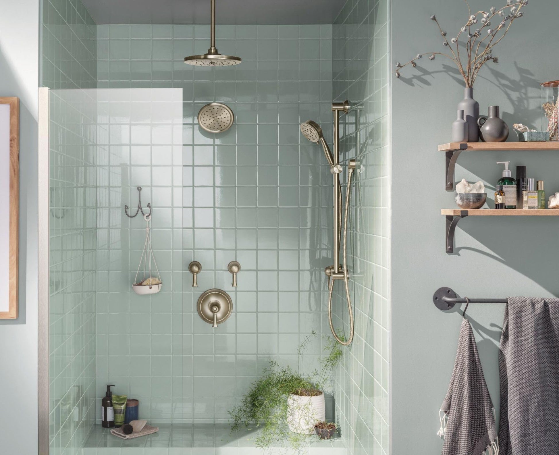 Brushed nickel shower arm flange mounted on tiled wall with showerhead and handheld spray fixture.