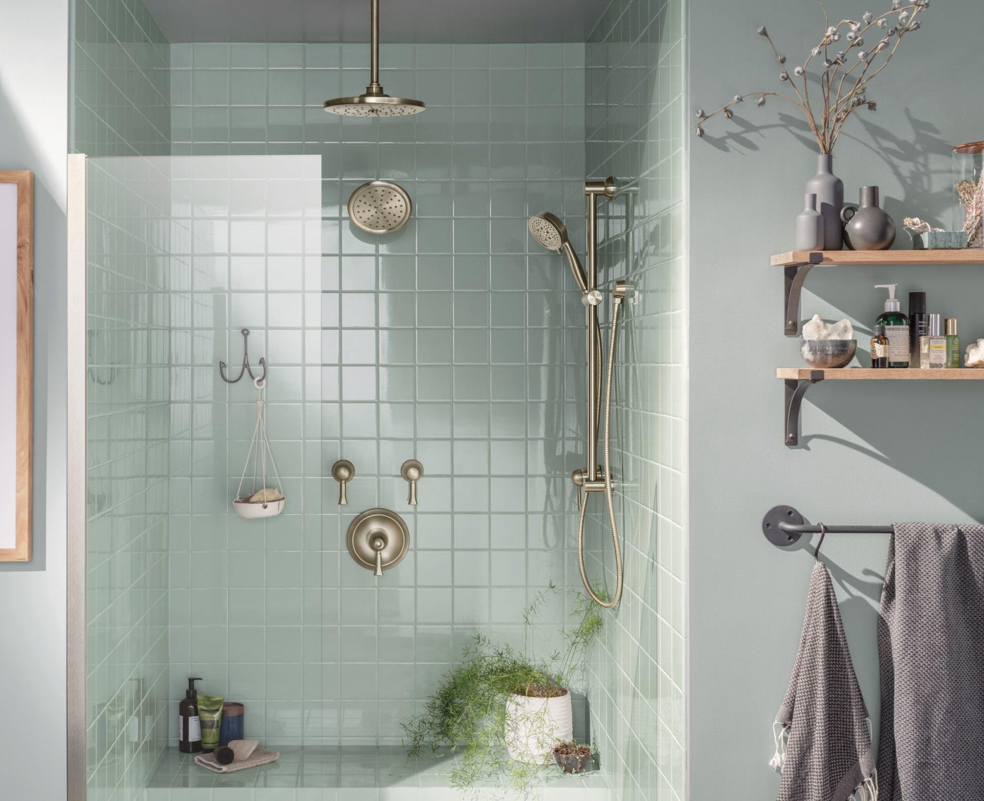 Brushed nickel shower arm flange mounted on tiled wall with showerhead and handheld spray fixture.