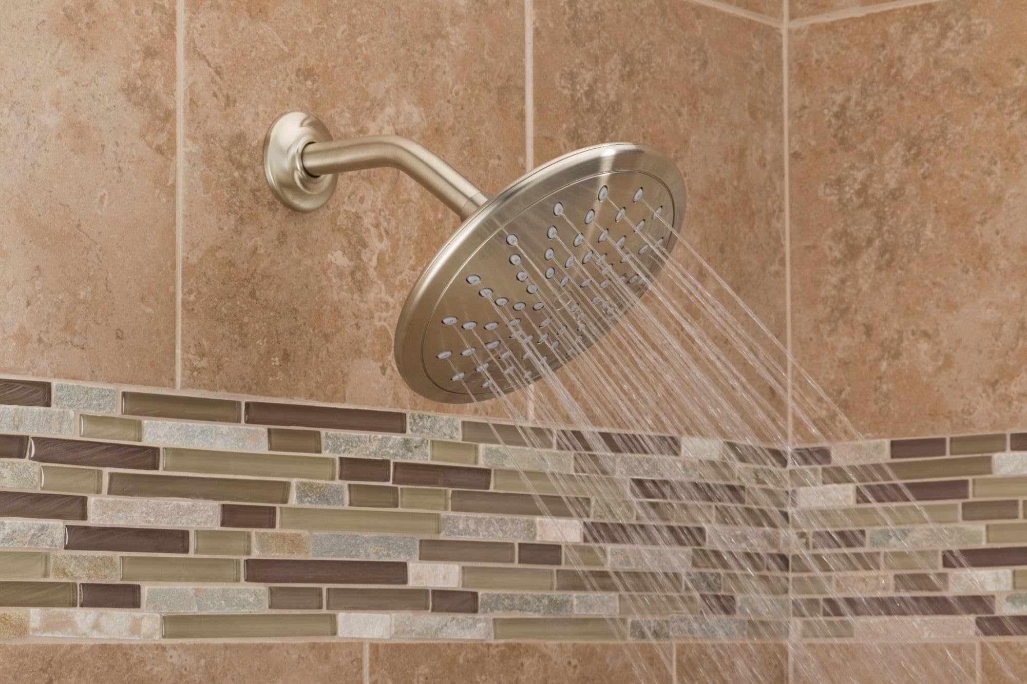Brushed nickel round rain shower head mounted on wall with curved arm, water spraying downward in bathroom with tile surround