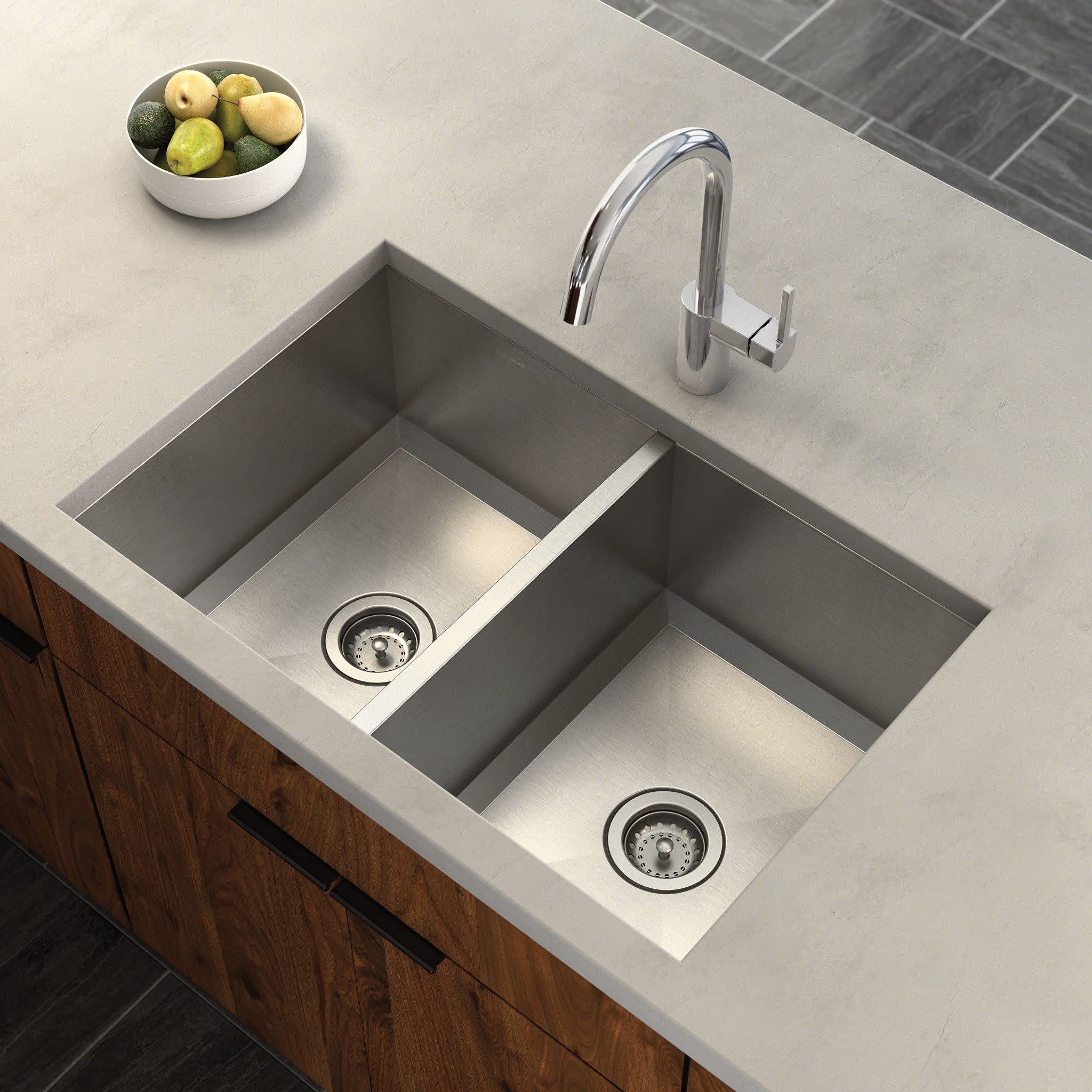 Chrome high-arc kitchen faucet with single handle mounted above a double-basin undermount sink in a light countertop.