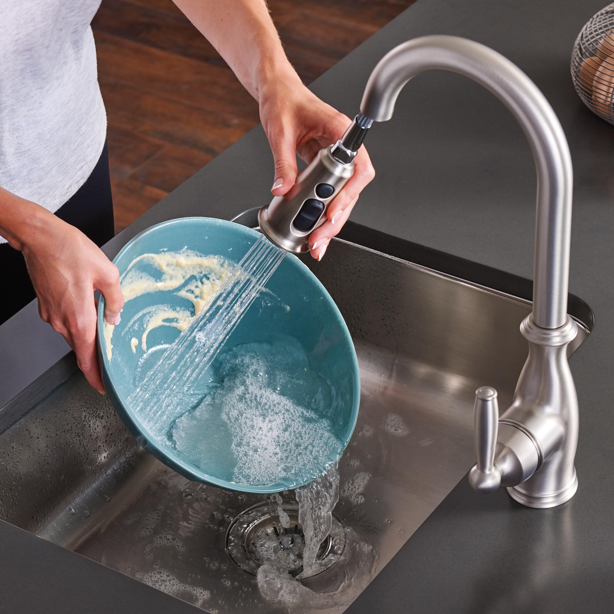 Stainless steel pull-down kitchen faucet with side handle spraying water into a blue bowl over sink.