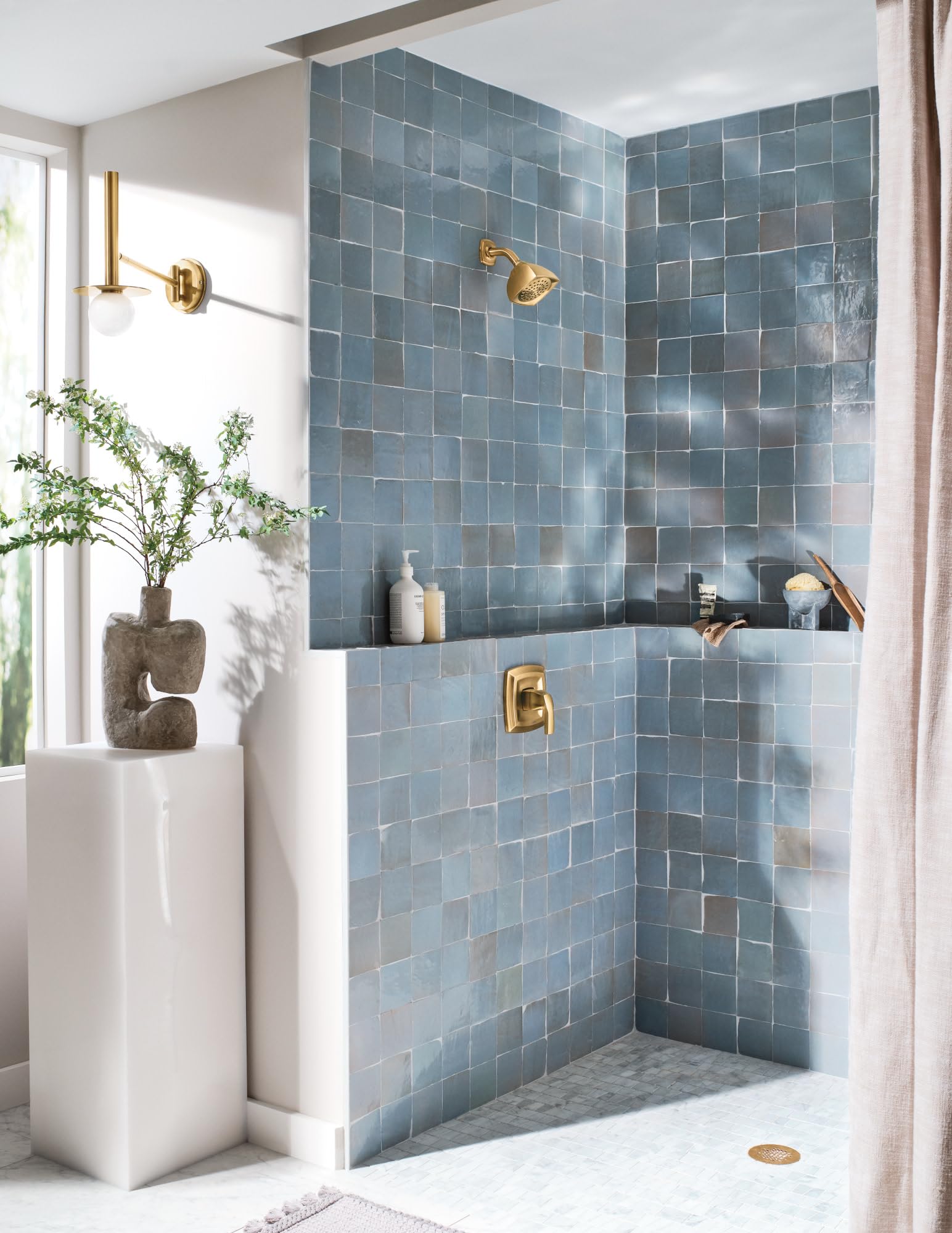Chrome shower valve and showerhead mounted on blue tile shower wall with gold accents.