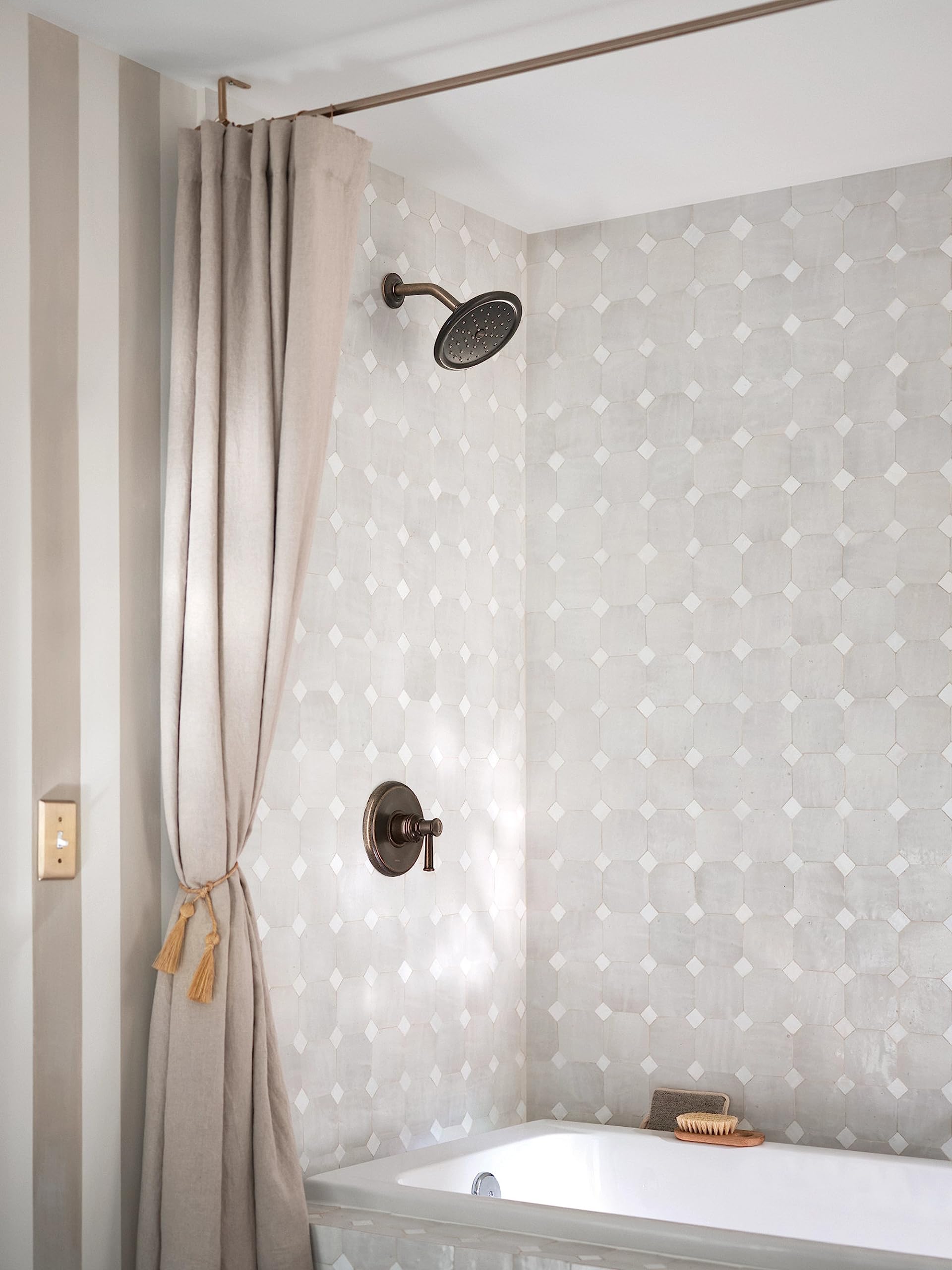Oil rubbed bronze shower trim with single handle control, round showerhead, and curved arm mounted on white diamond tile bath