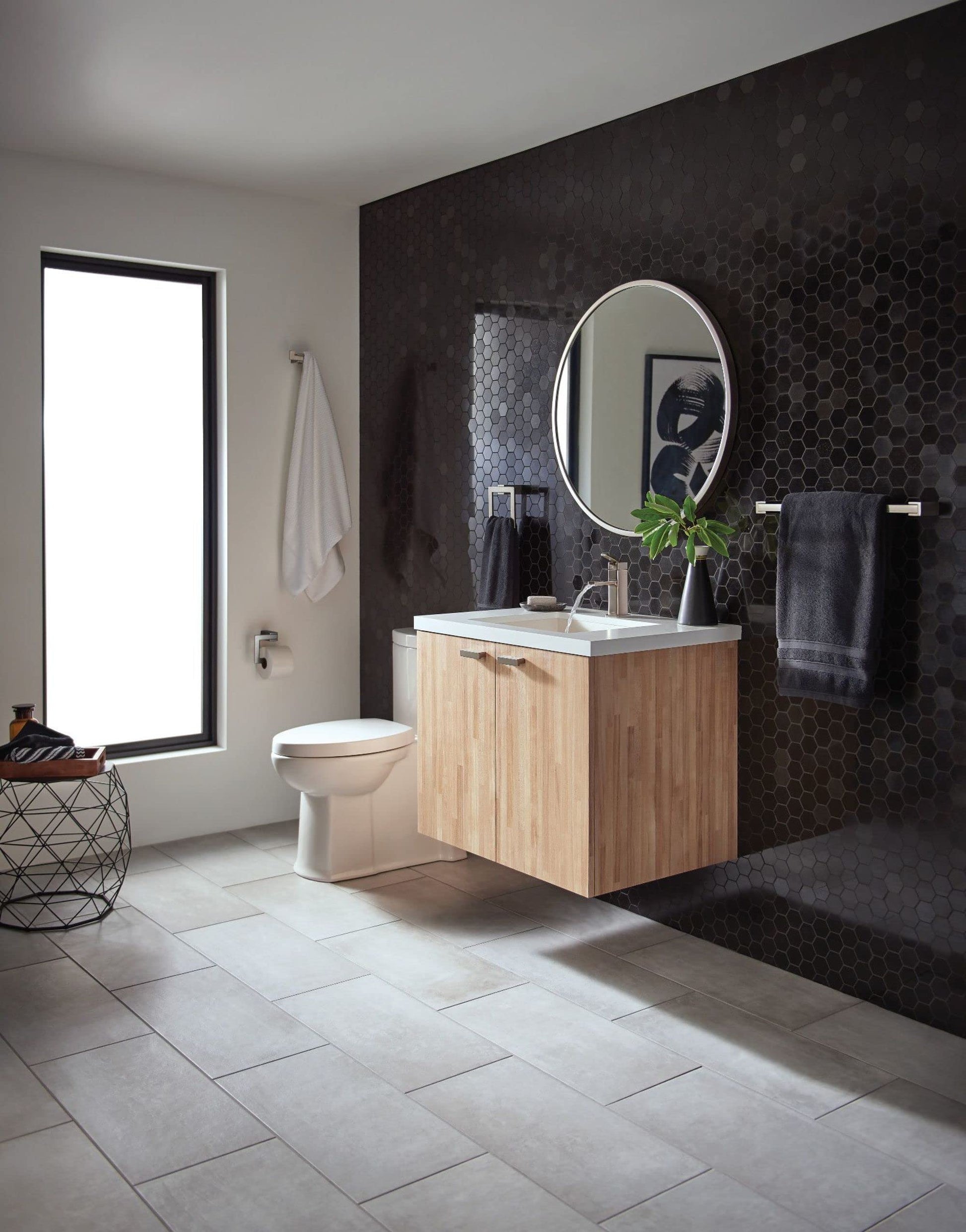 Brushed nickel double robe hook mounted on dark hexagonal tile wall above bathroom sink vanity.