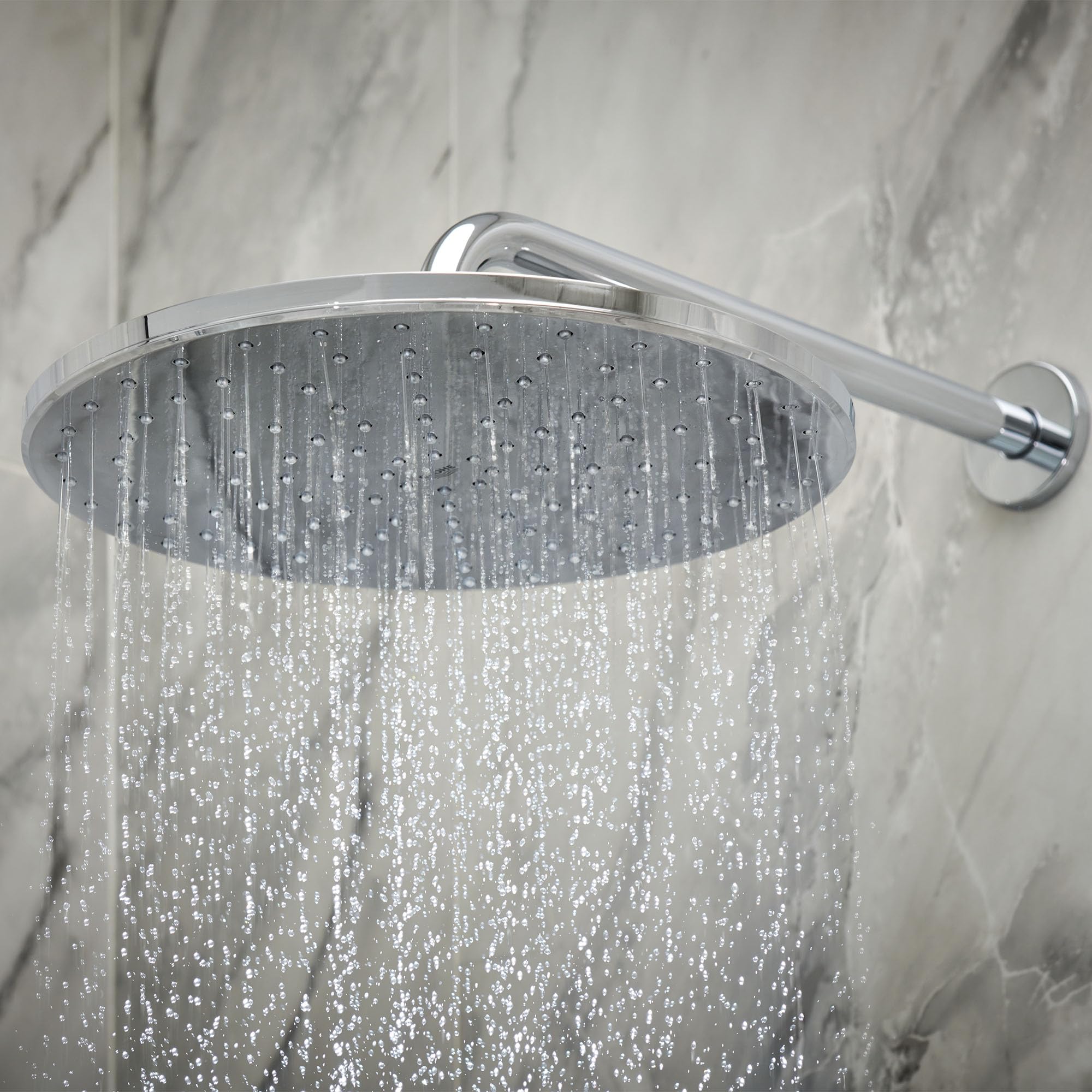 Chrome rain showerhead with wall-mounted arm and control valve, water streaming downward against marble tile background.