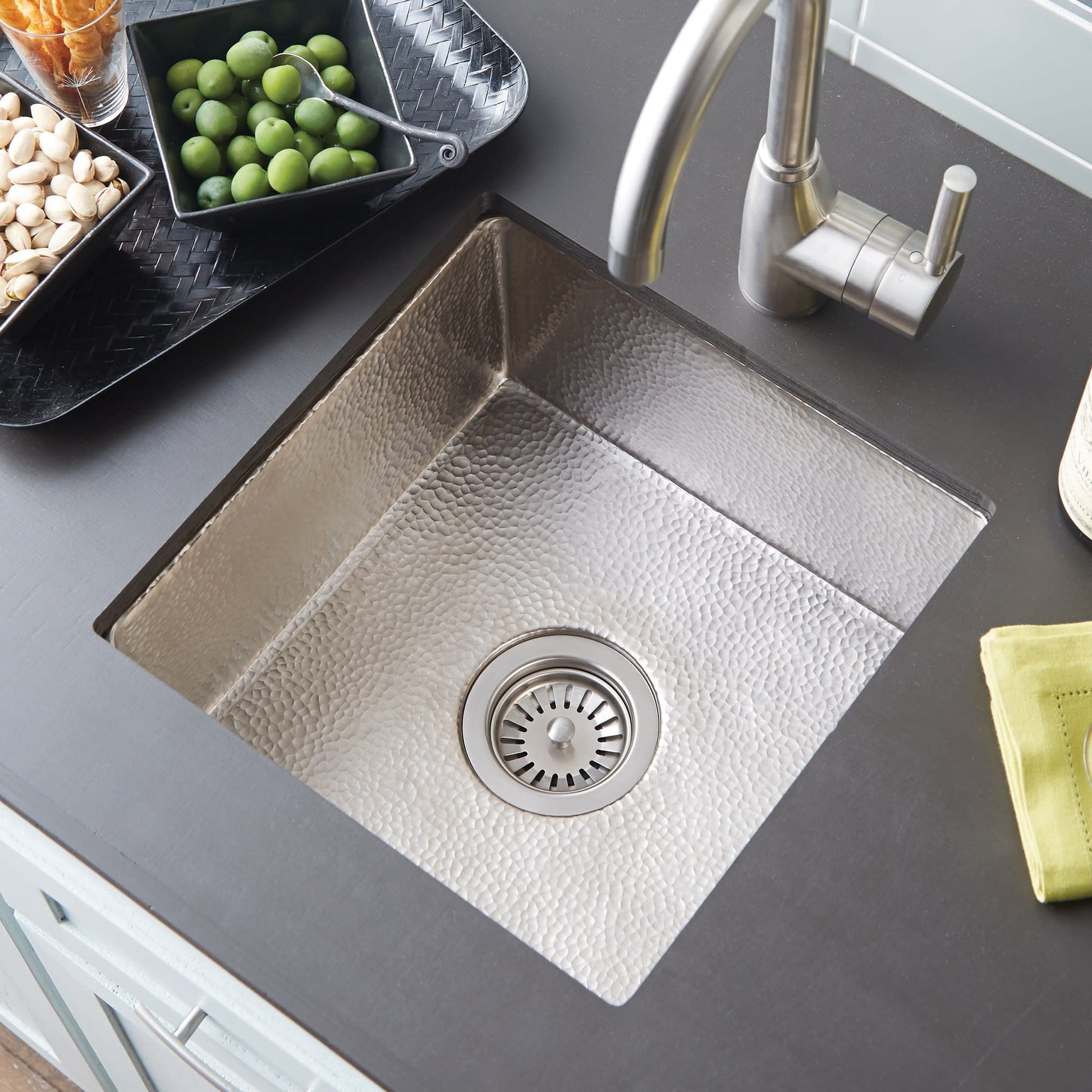 Polished copper prep sink with hammered texture and drain, paired with stainless steel faucet on gray countertop.