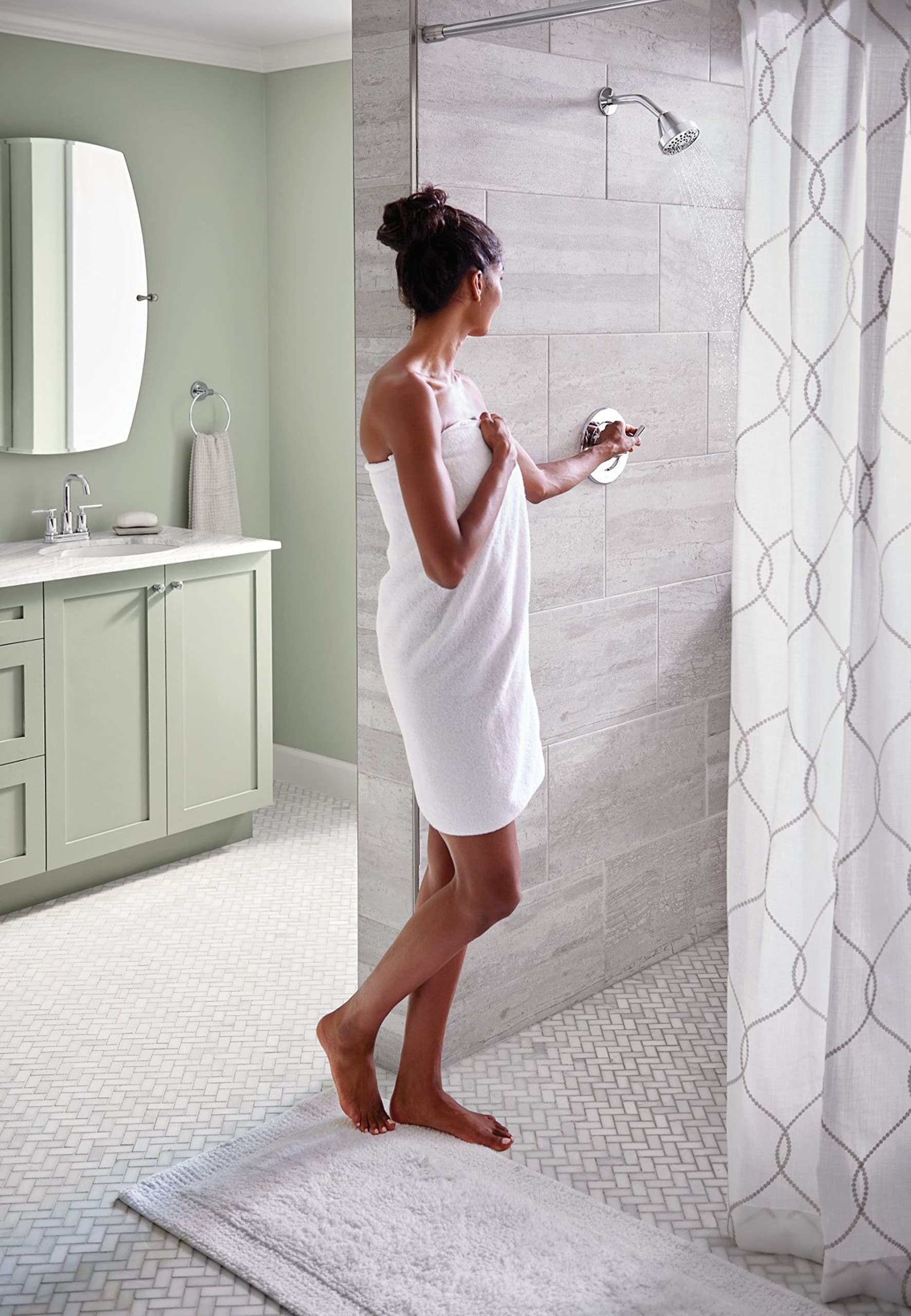 Chrome shower valve trim with round showerhead mounted on gray tile wall in bathroom setting.