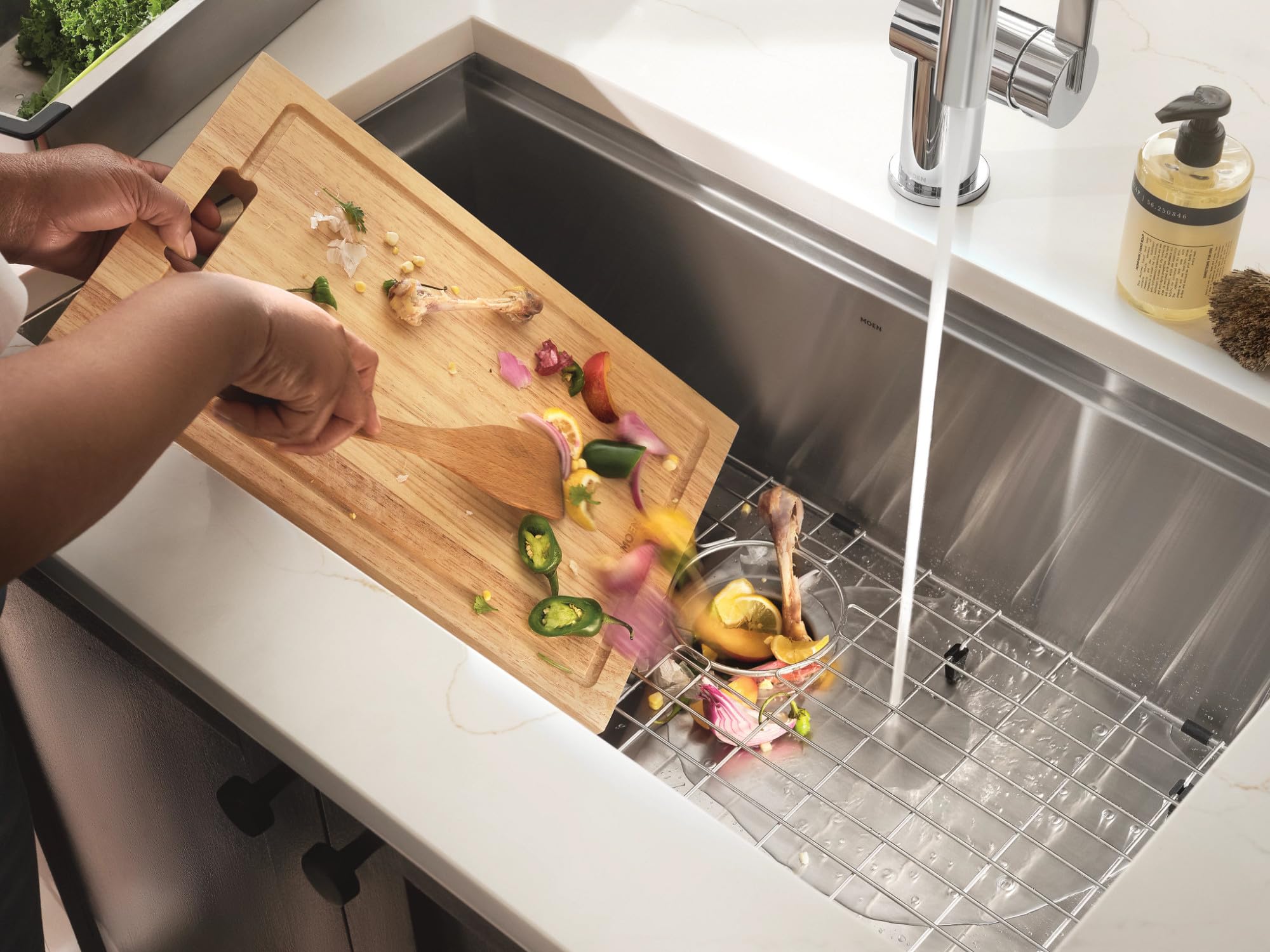 Stainless steel garbage disposal installed in sink with food scraps being scraped from wooden cutting board into the drain.