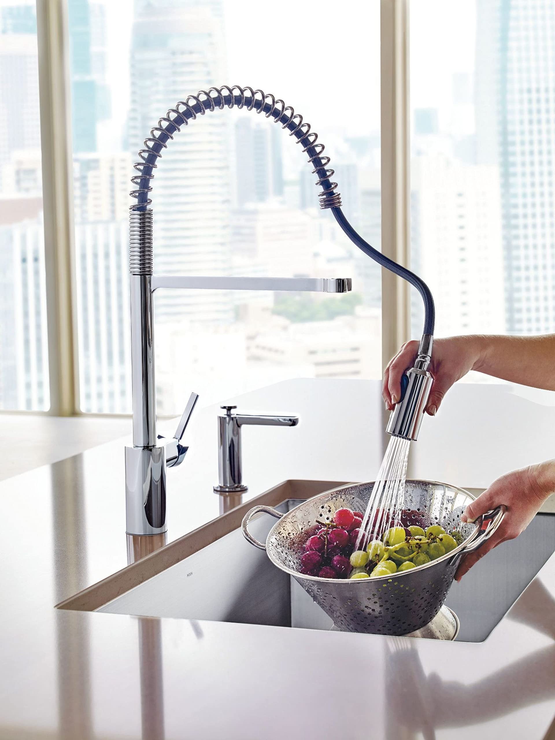 Chrome pulldown kitchen faucet with coiled hose sprayer extended over sink rinsing berries.