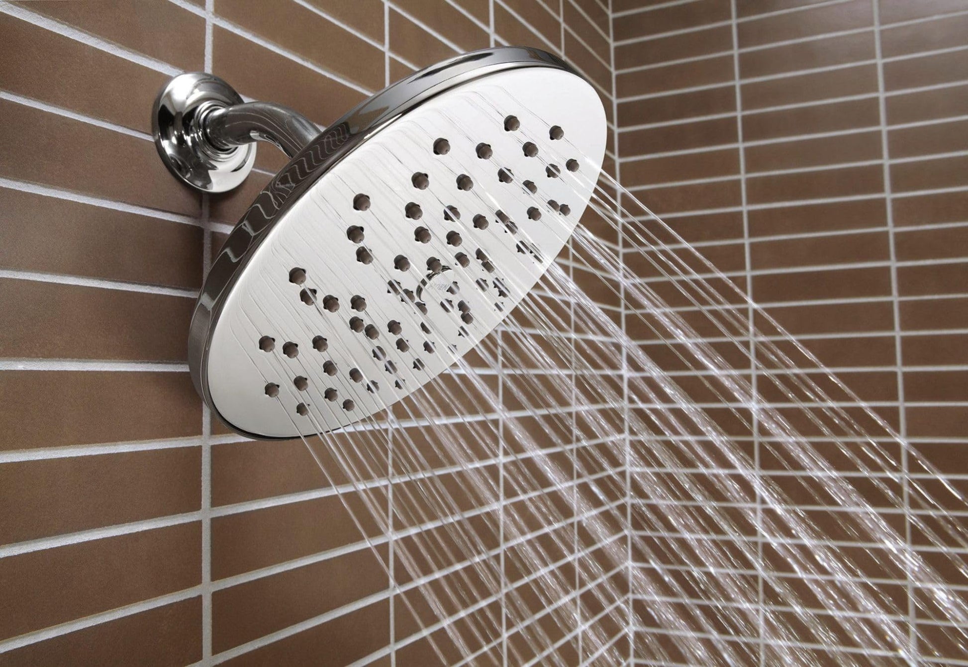Large round showerhead with multiple spray holes mounted on wall with chrome arm, water streams visible.