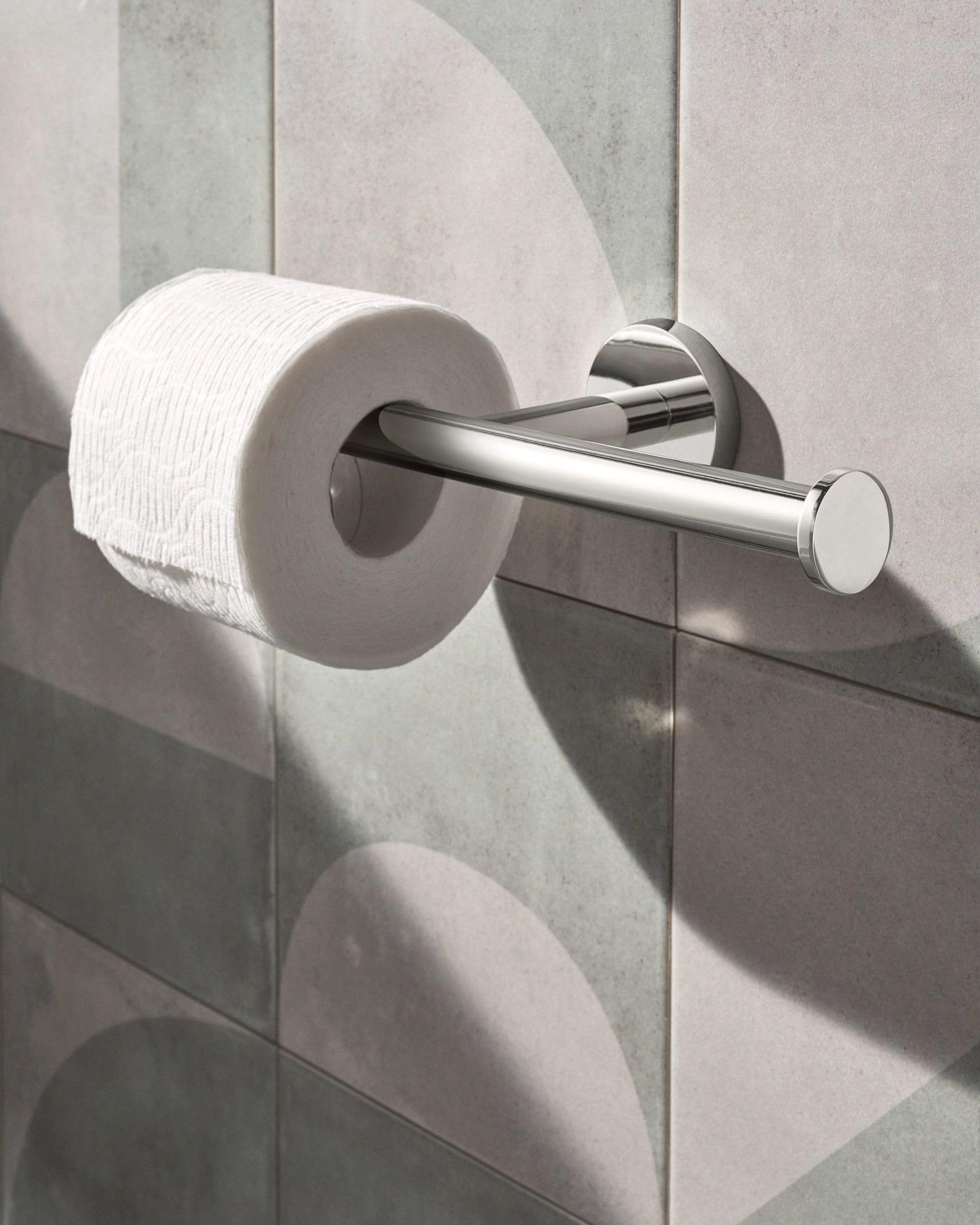 Chrome double toilet paper holder with horizontal bar mounted on gray tile wall with one roll installed.