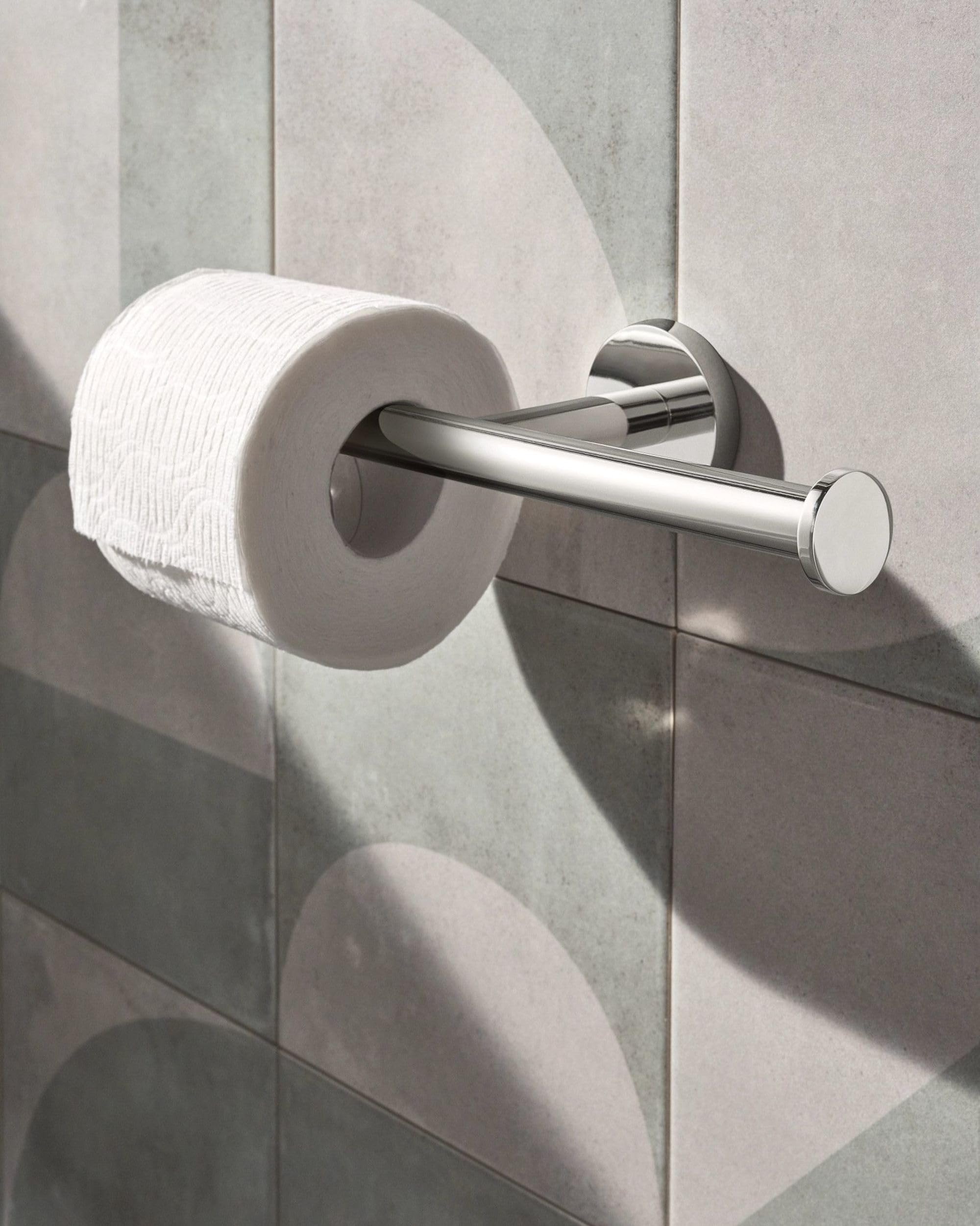 Chrome double toilet paper holder with horizontal bar mounted on gray tile wall with one roll installed.