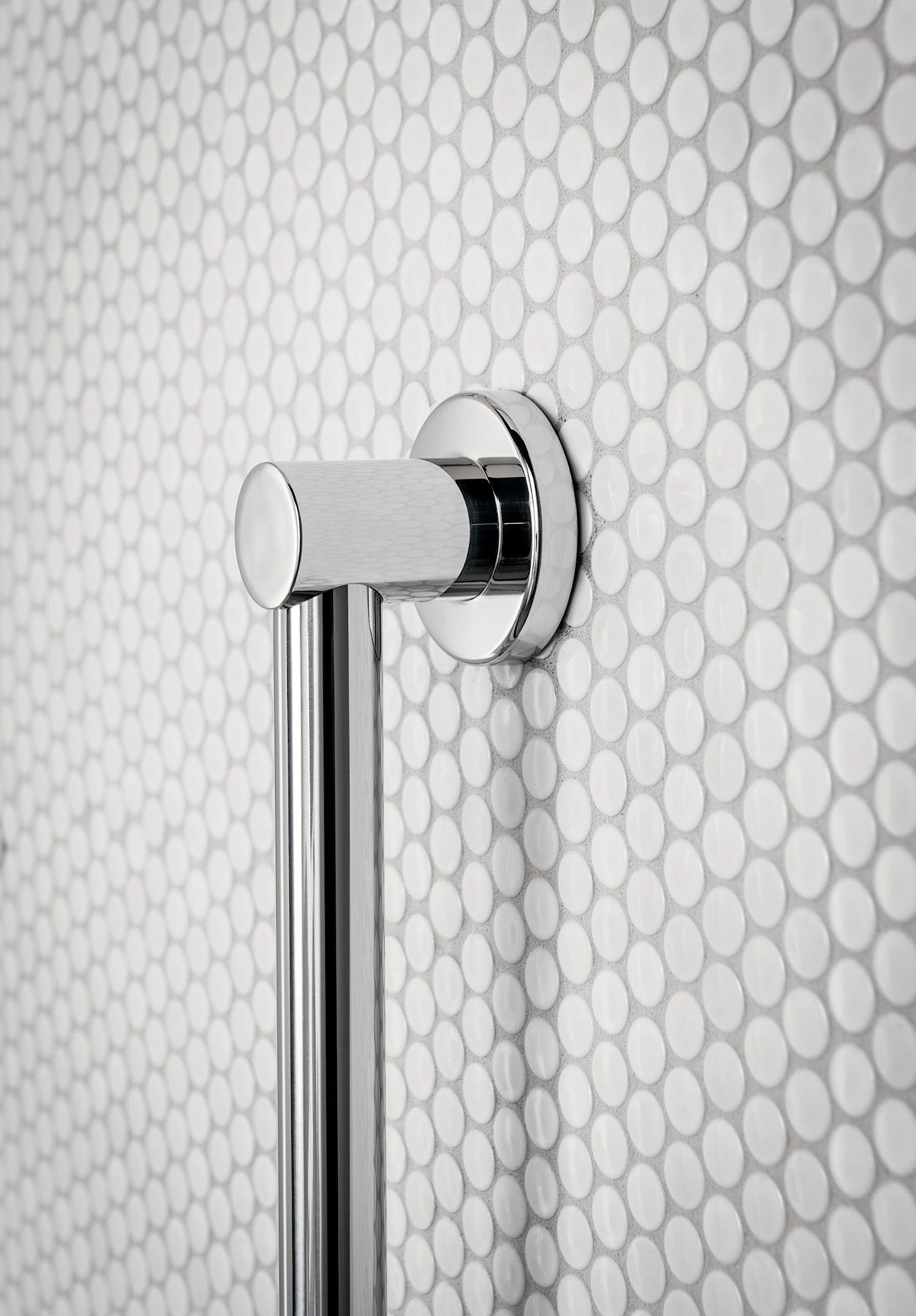 Chrome stainless steel grab bar with cylindrical handle mounted vertically on white penny tile bathroom wall.