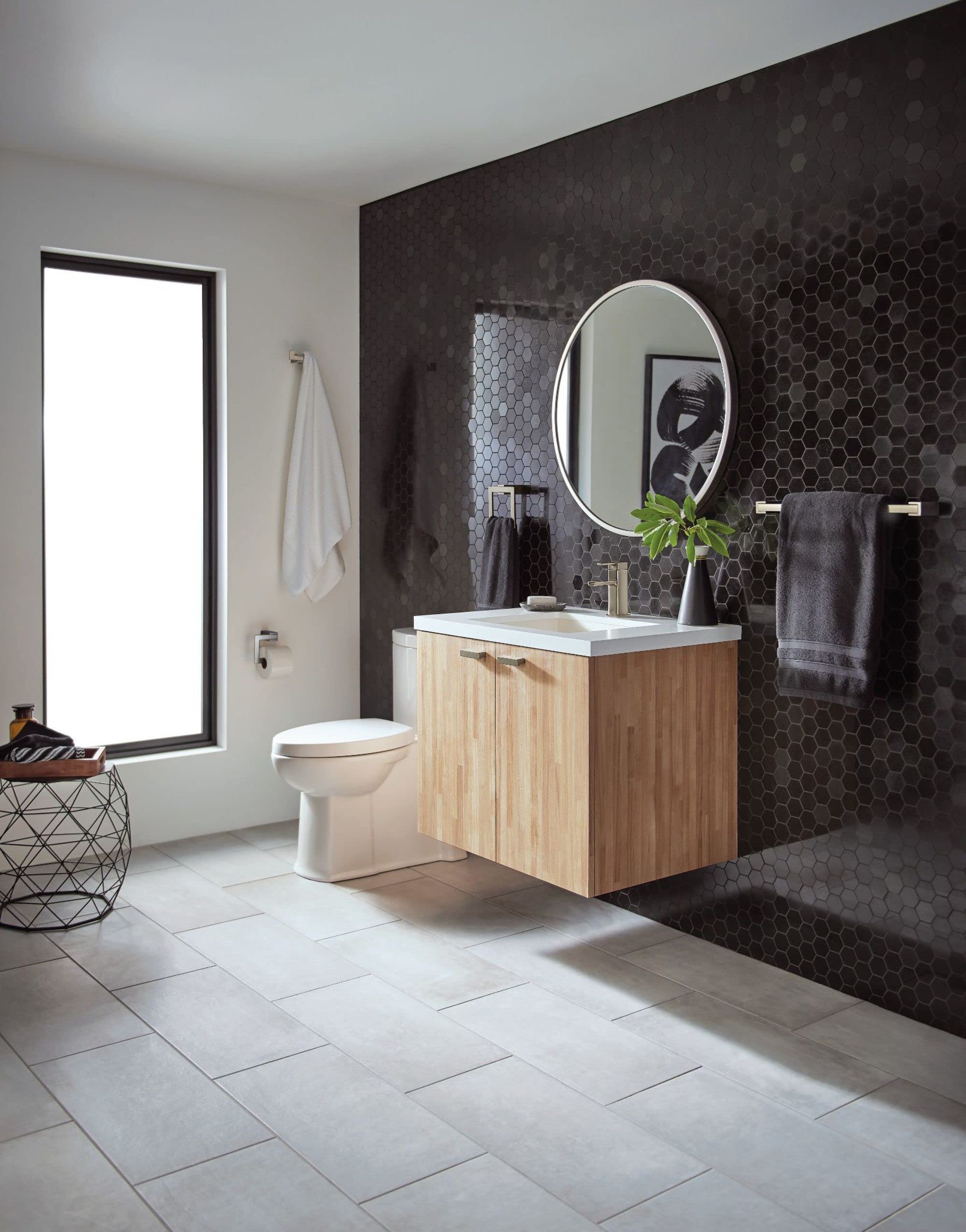Brushed nickel double robe hook mounted on dark hexagonal tile wall above bathroom sink vanity.