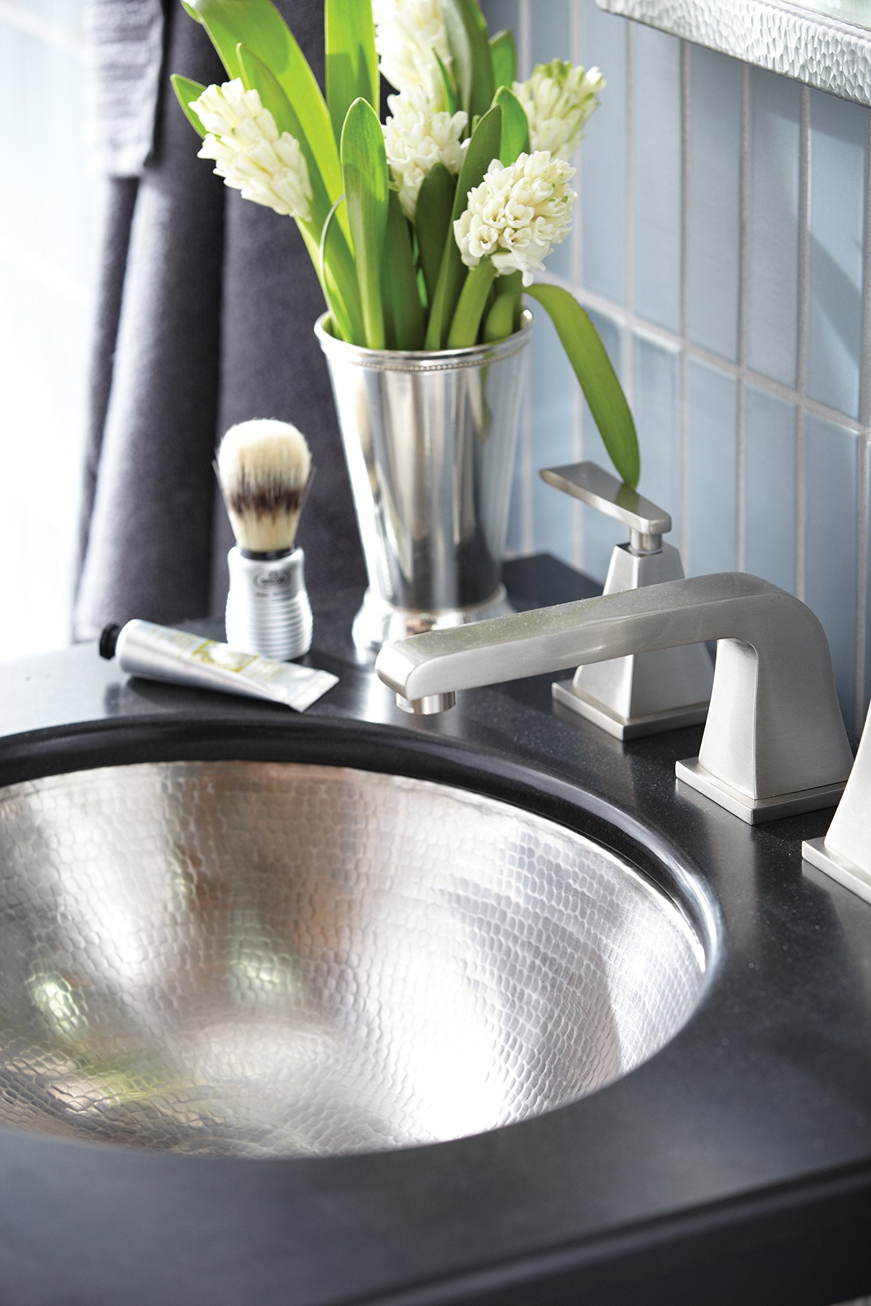 Hammered copper round bathroom sink with brushed nickel faucet and handles on dark countertop.