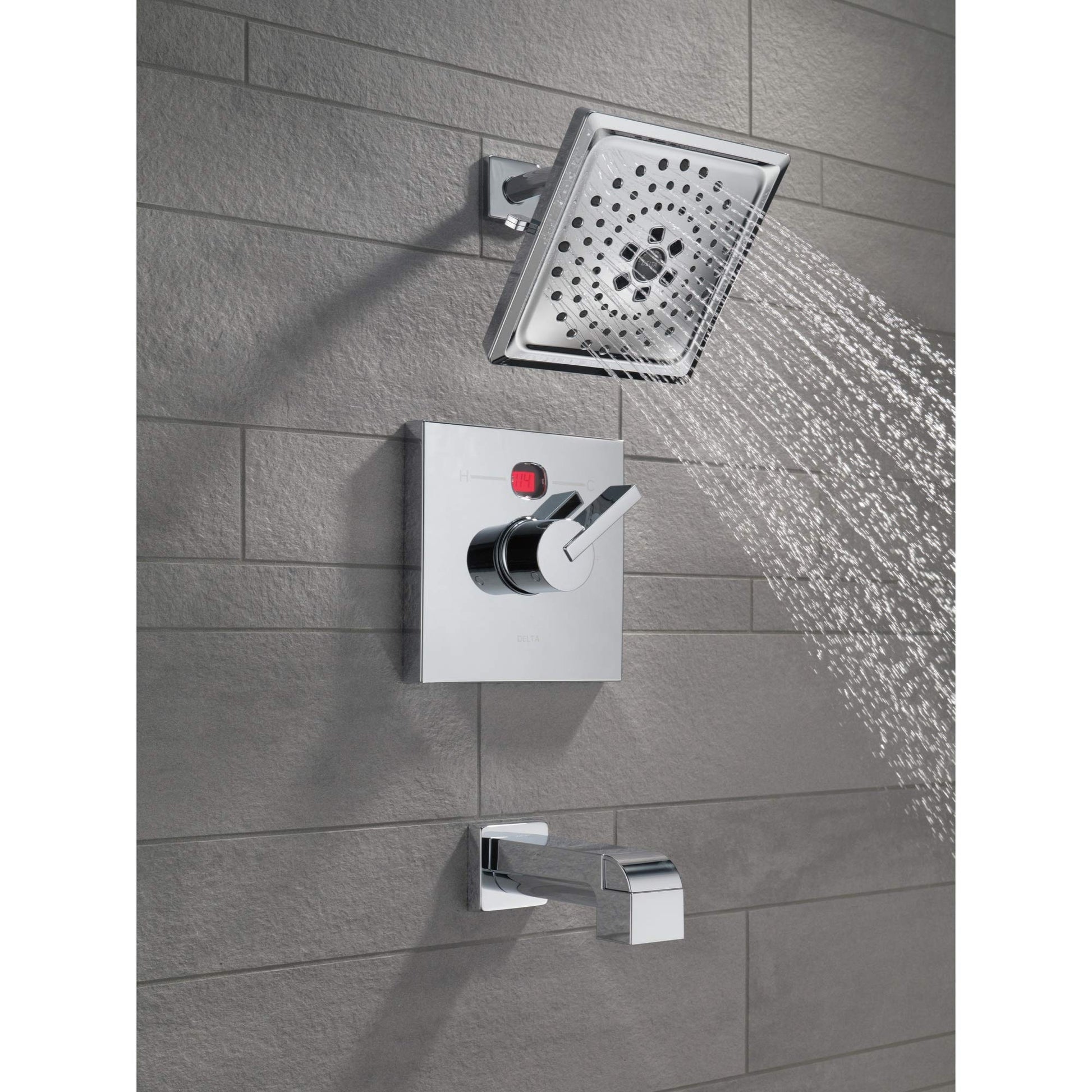 Chrome tub spout with pull-up diverter mounted on gray tile wall with shower head and control valve above.