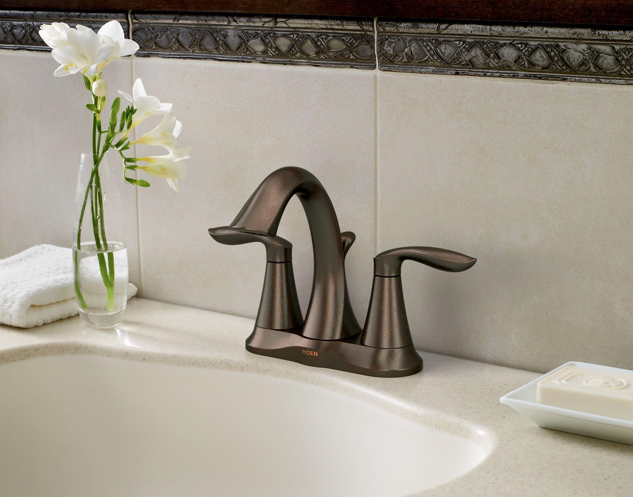 Oil rubbed bronze two-handle bathroom faucet with curved spout and lever handles on white sink countertop.