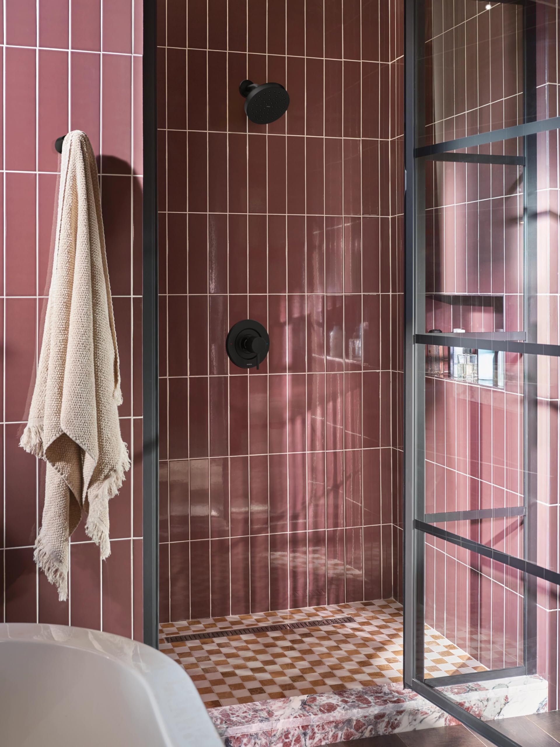 Matte black robe hook mounted on burgundy tile wall in shower enclosure with towel hanging.