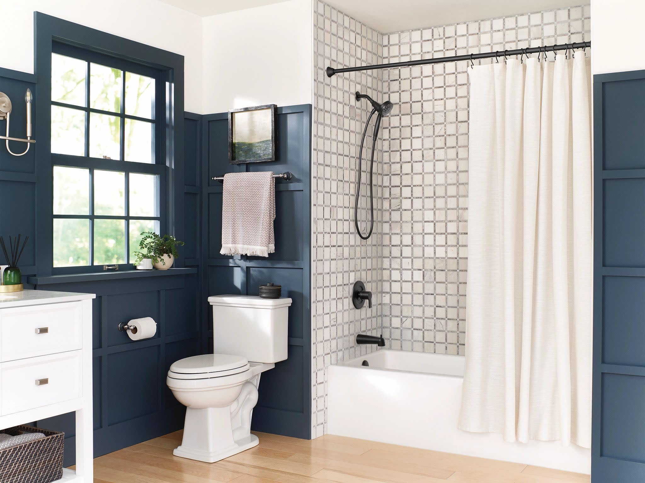 Matte black hand shower mounted on shower wall with curved arm and matching valve trim.