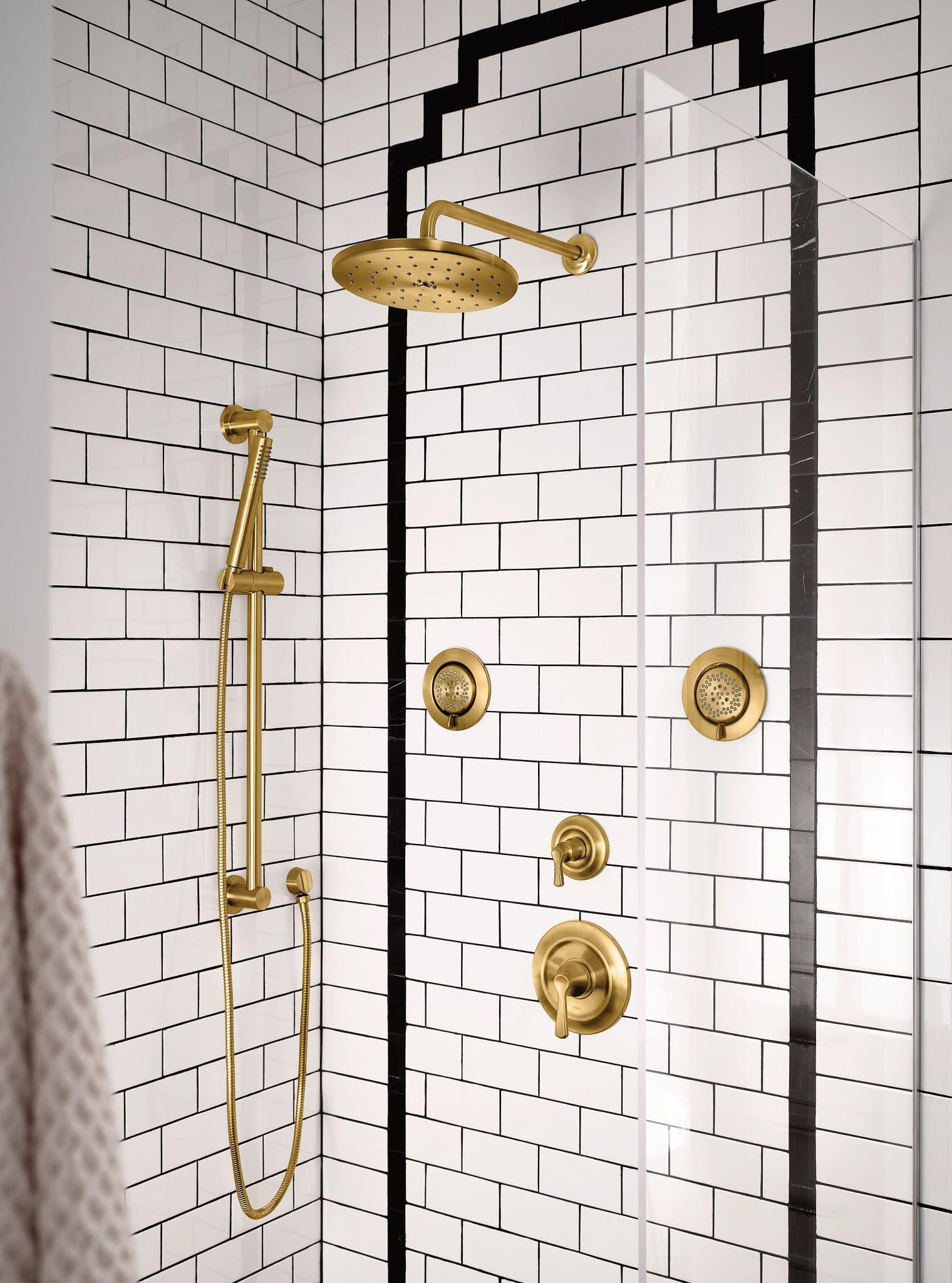 Brushed gold shower arm with circular flange mounted to tile wall, extending from wall to overhead showerhead.