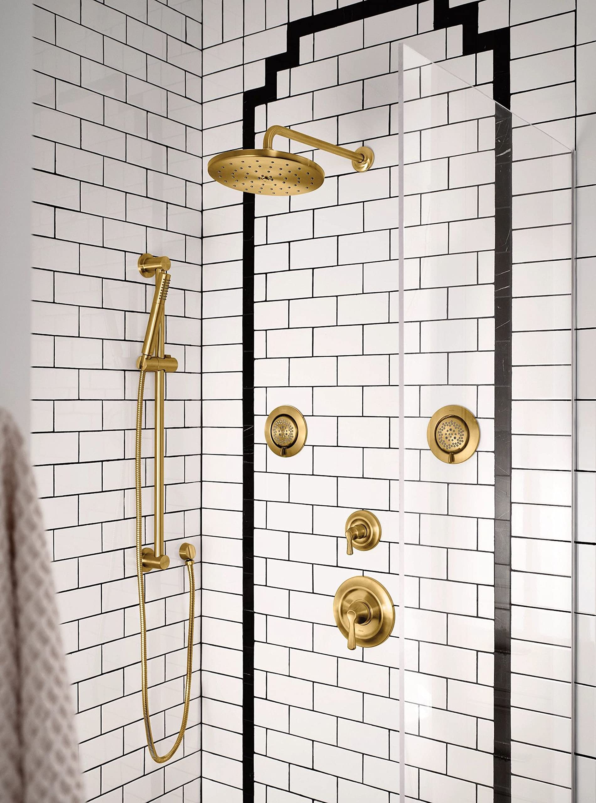 Brushed gold shower system with overhead rain showerhead, handheld wand, and multiple body jets mounted on white subway tile 