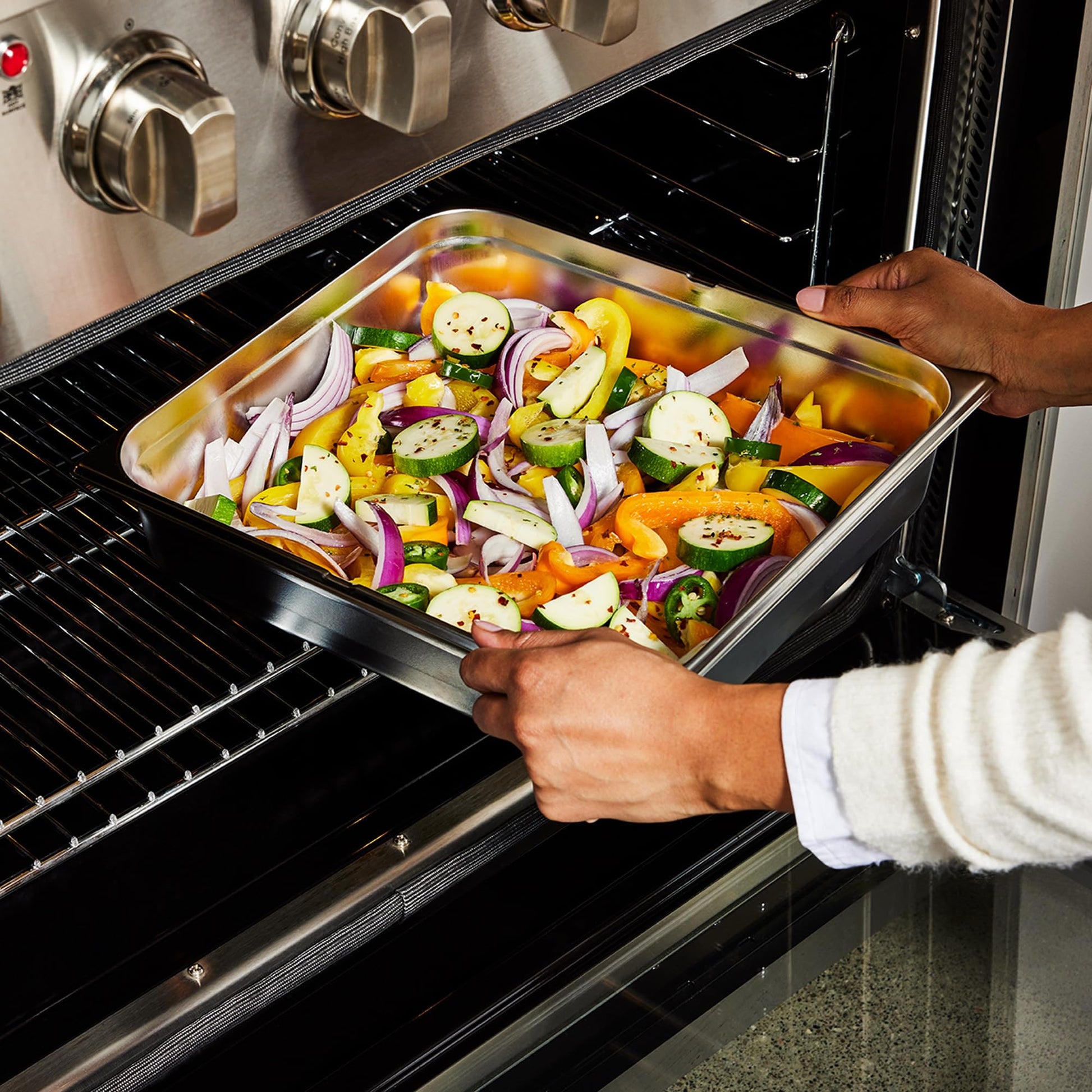 Stainless steel rectangular sink tray filled with sliced vegetables being placed in an oven.