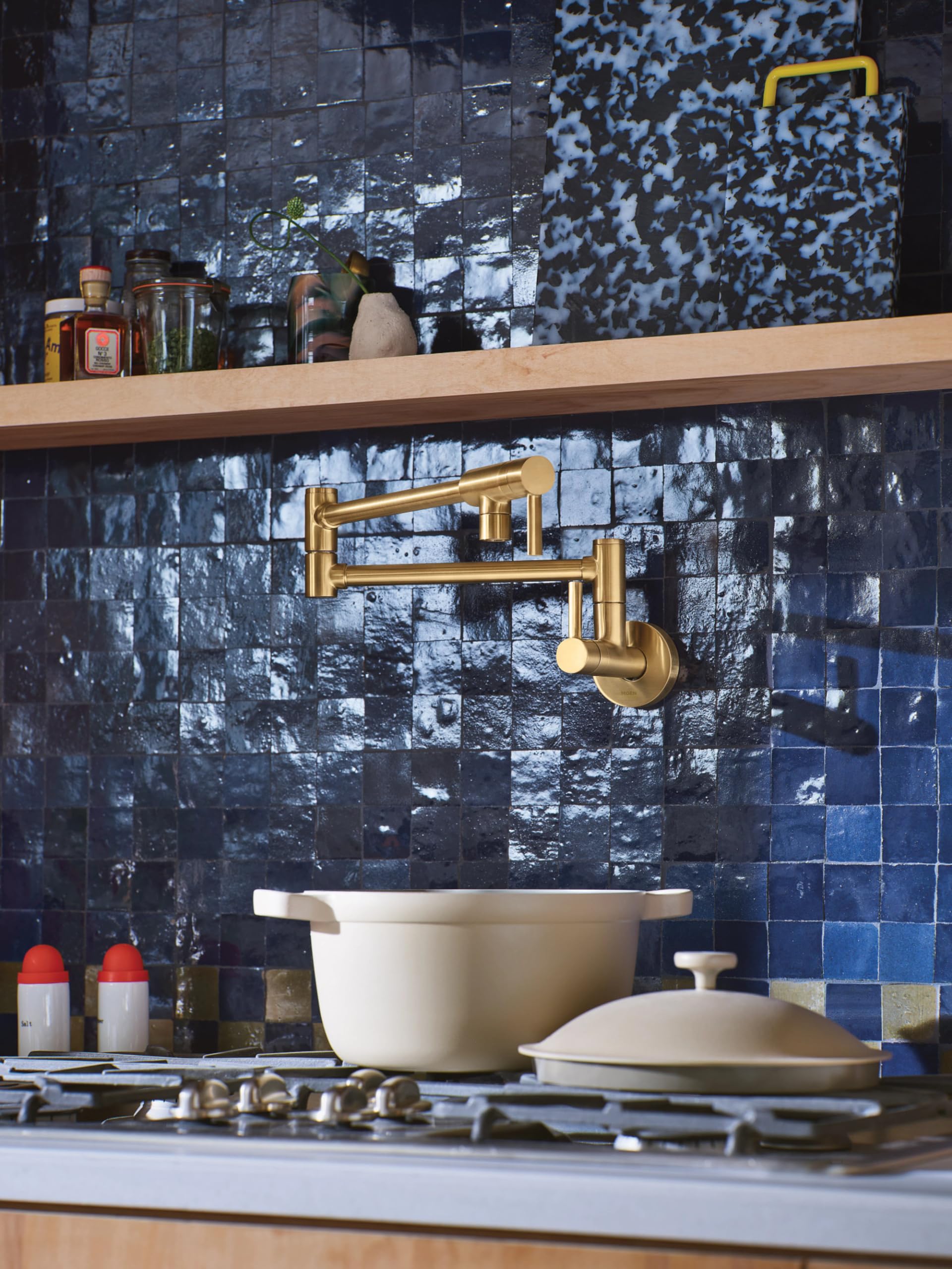 Brushed gold wall-mounted pot filler faucet with double-jointed swing arm extended over white cookware on stovetop.