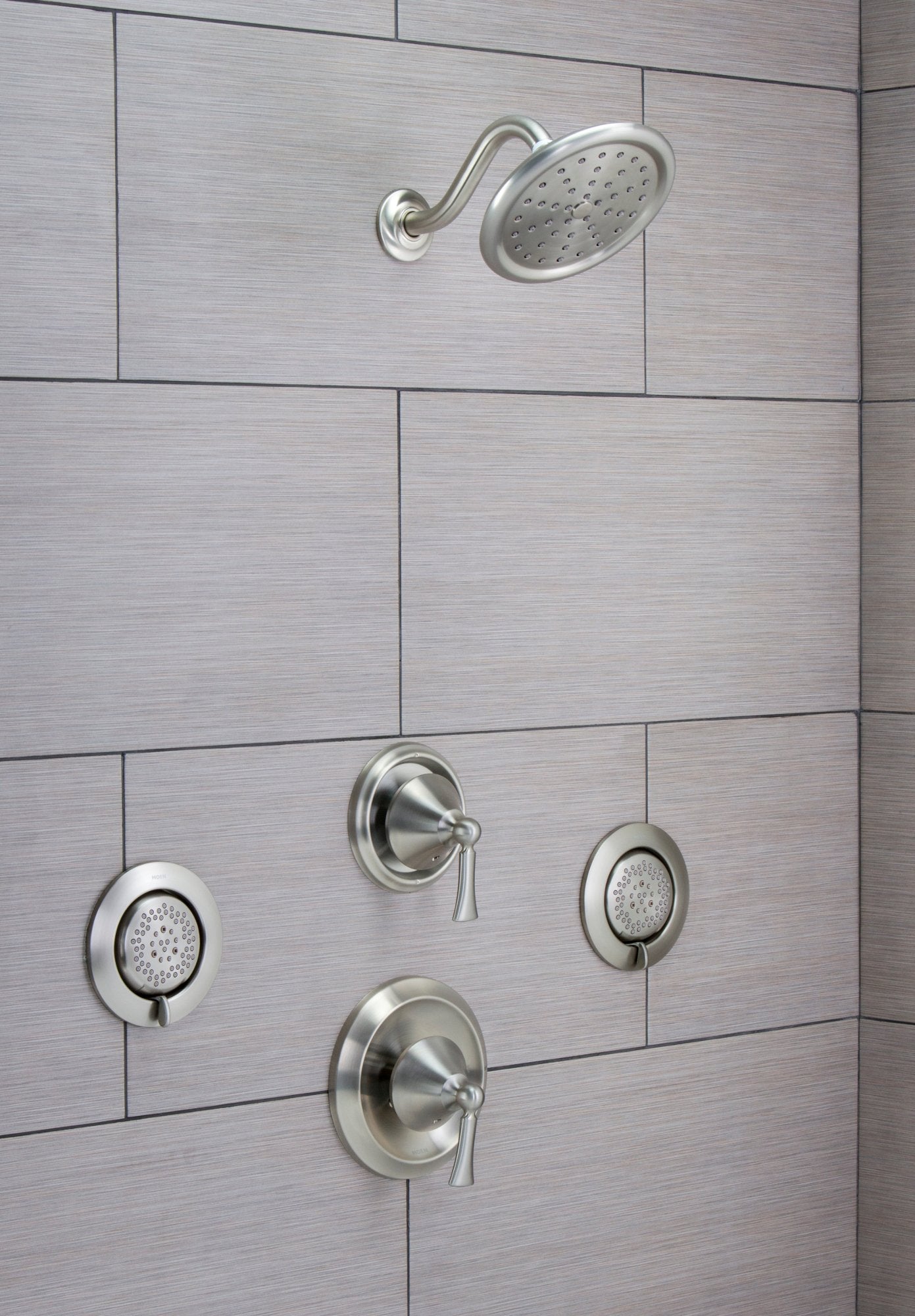 Chrome body spray system mounted on tile wall with overhead showerhead and two handheld spray jets with control valves.