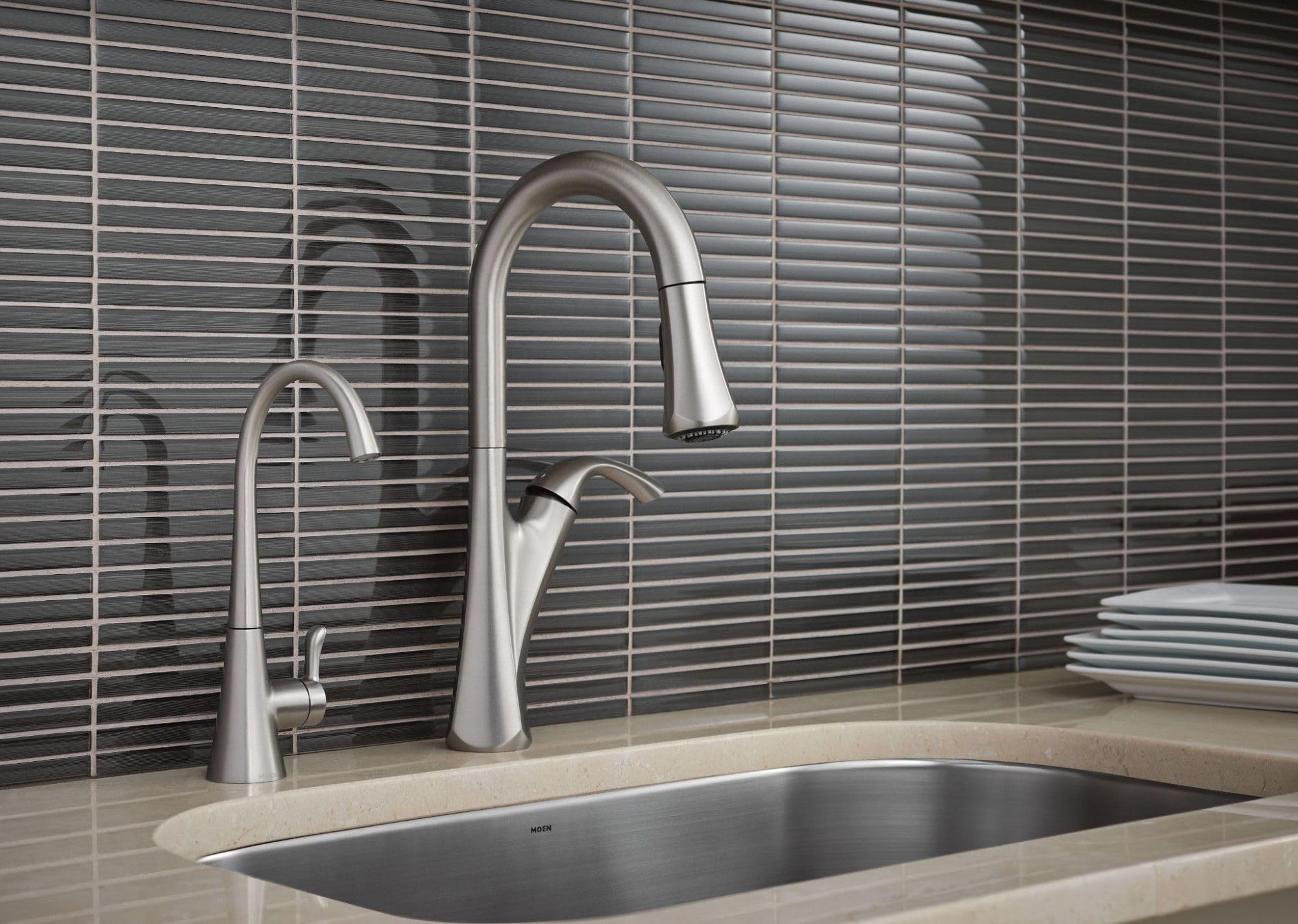 Stainless steel kitchen faucet with curved spout and pull-down sprayer mounted above rectangular sink on tiled backsplash.