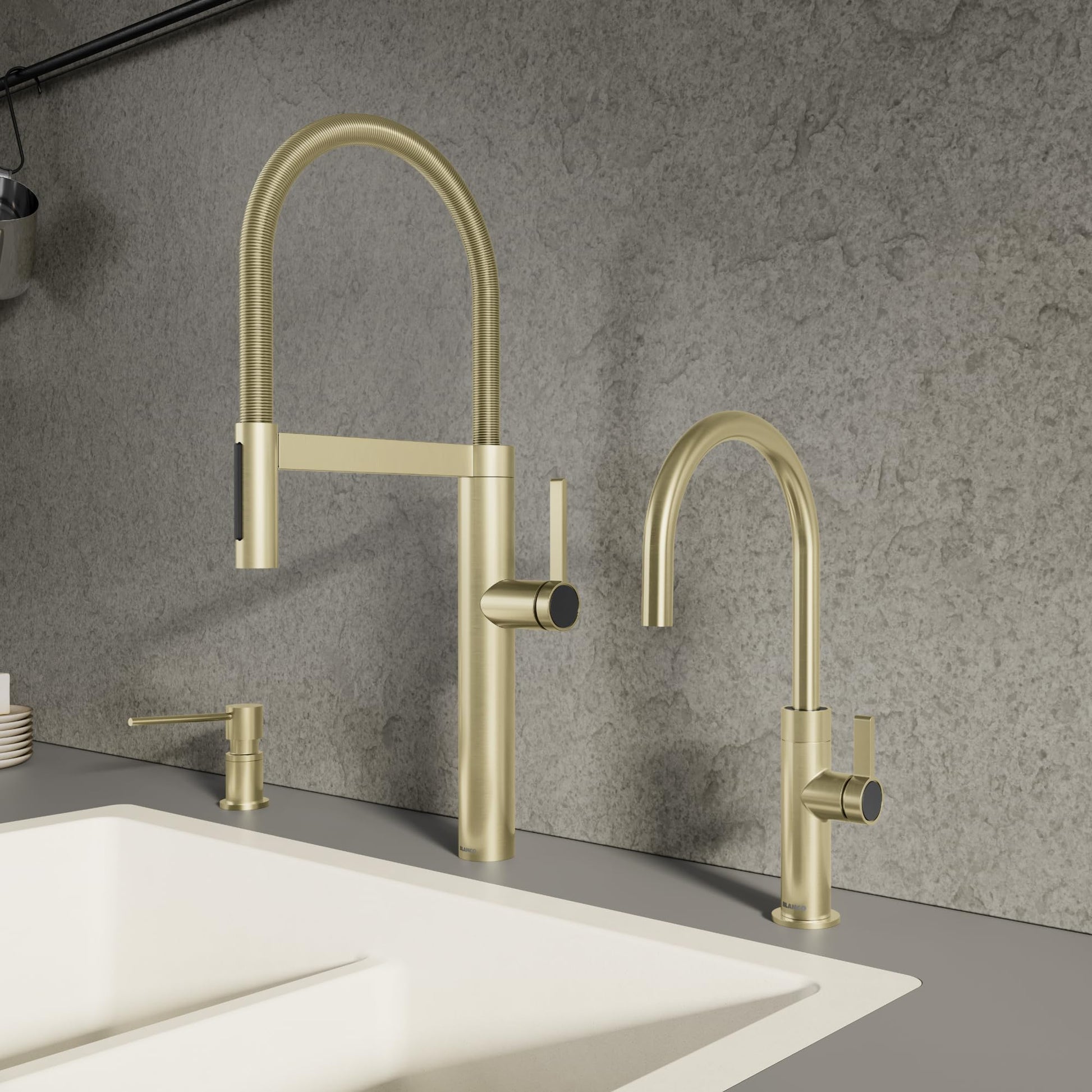 Satin gold pull-down kitchen faucet with curved spout and matching smaller faucet on gray countertop.