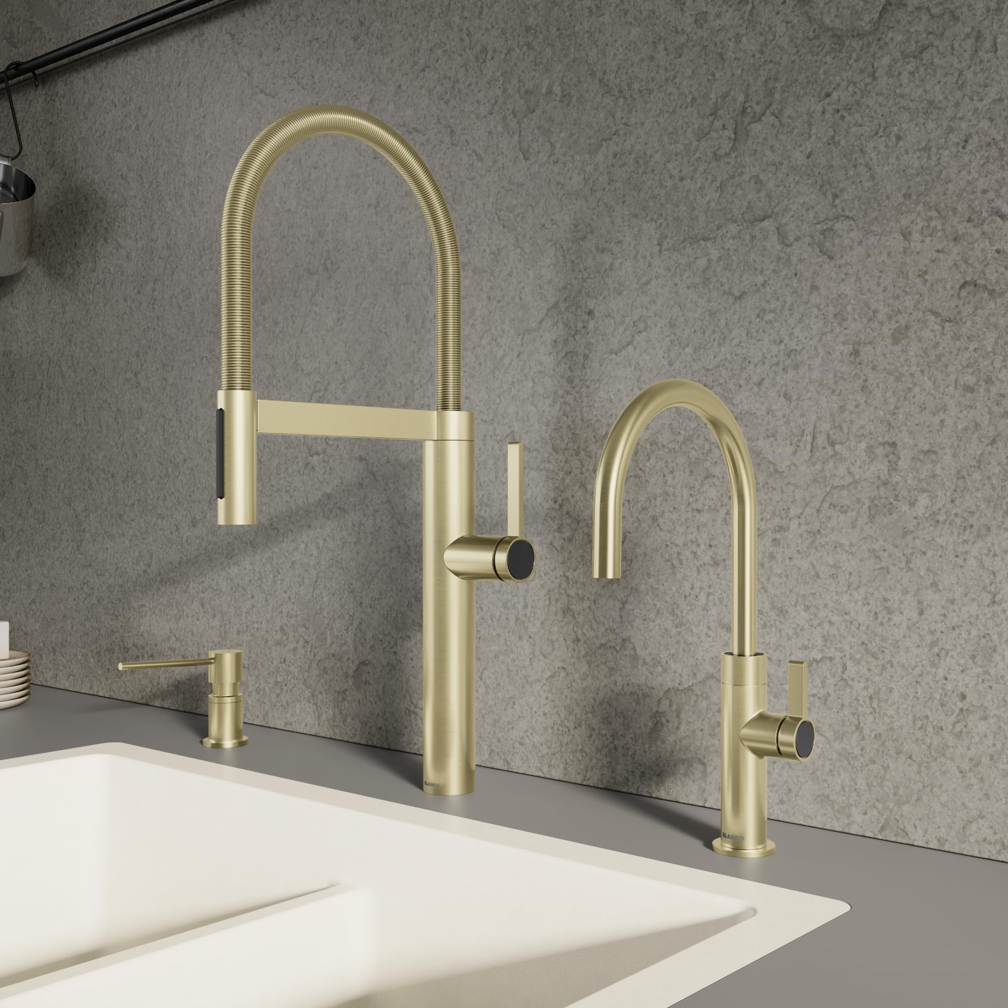 Satin gold pull-down kitchen faucet with curved spout and matching smaller faucet on gray countertop.