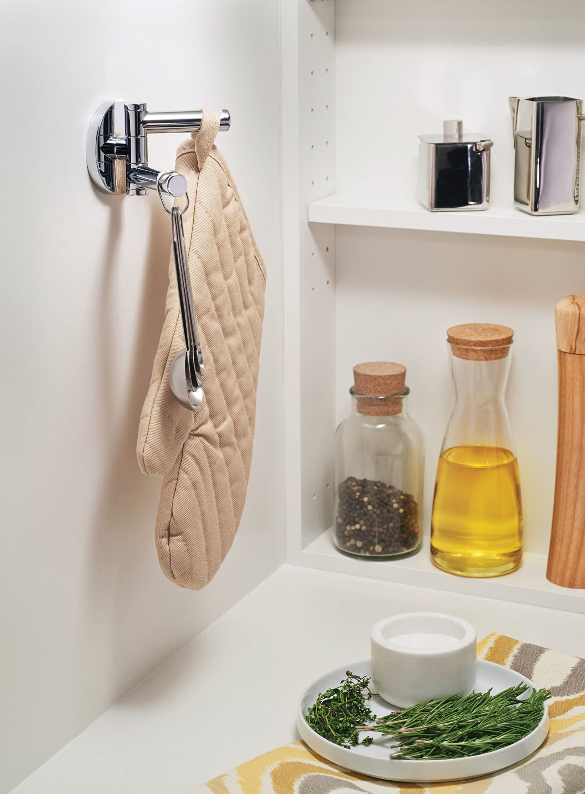 Chrome double swivel robe hook mounted on white wall with beige kitchen towel hanging from one arm.