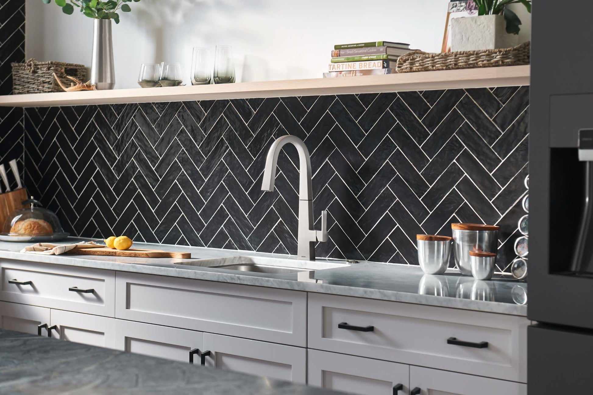 Stainless steel pull-down kitchen faucet with curved spout installed above sink in modern kitchen with herringbone tile backs