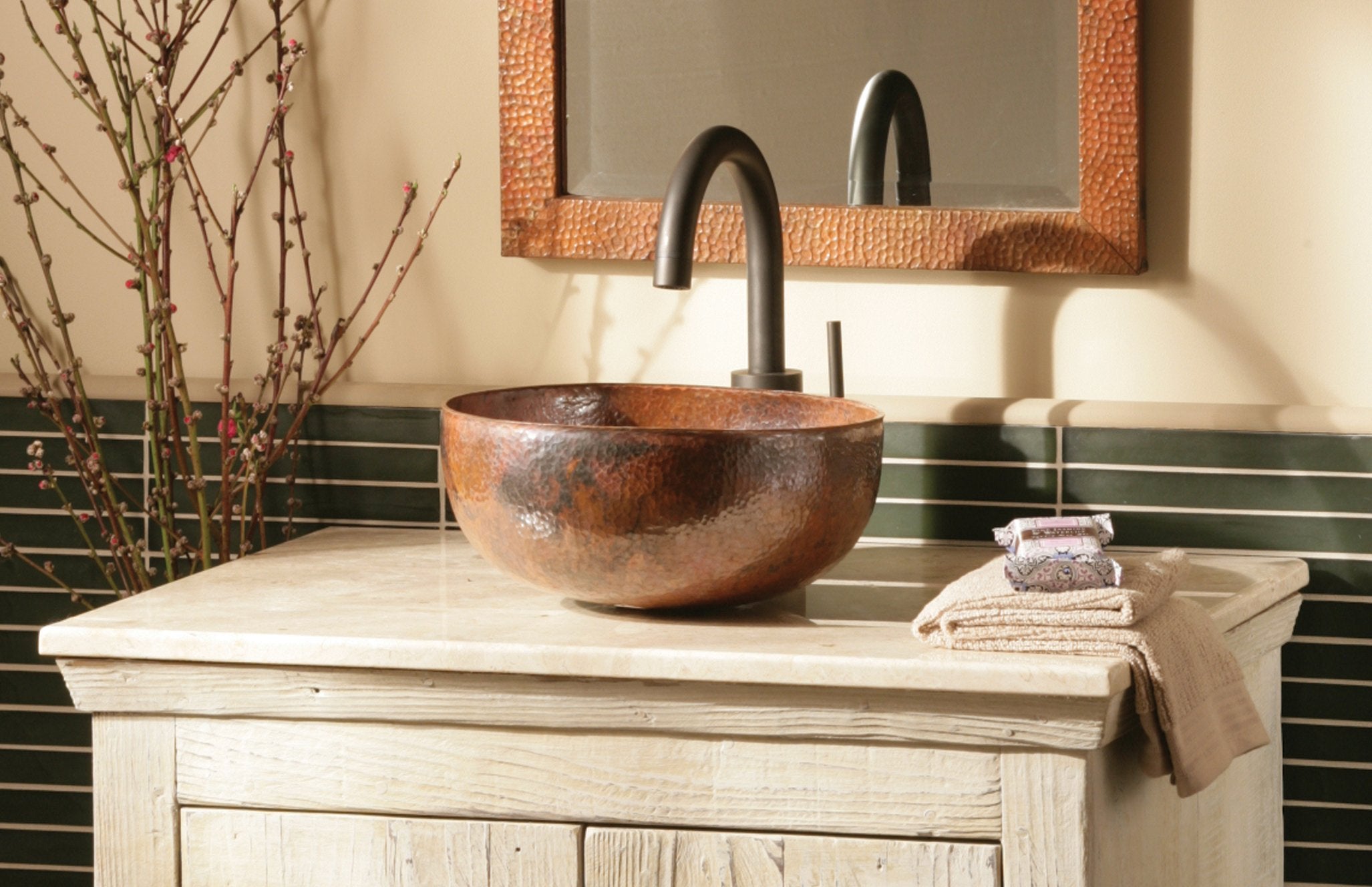 Hammered copper vessel sink with textured surface mounted on whitewashed wooden vanity with black faucet.