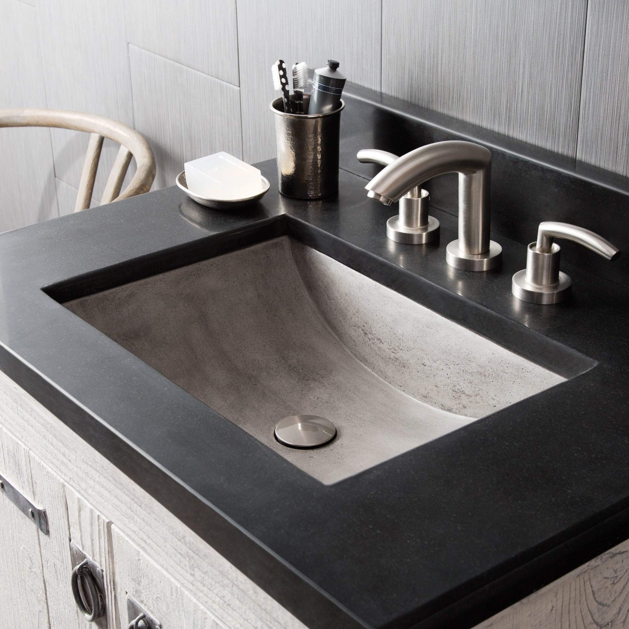 Slate-colored rectangular bathroom sink with stainless steel faucet and handles, mounted on dark countertop with accessories 
