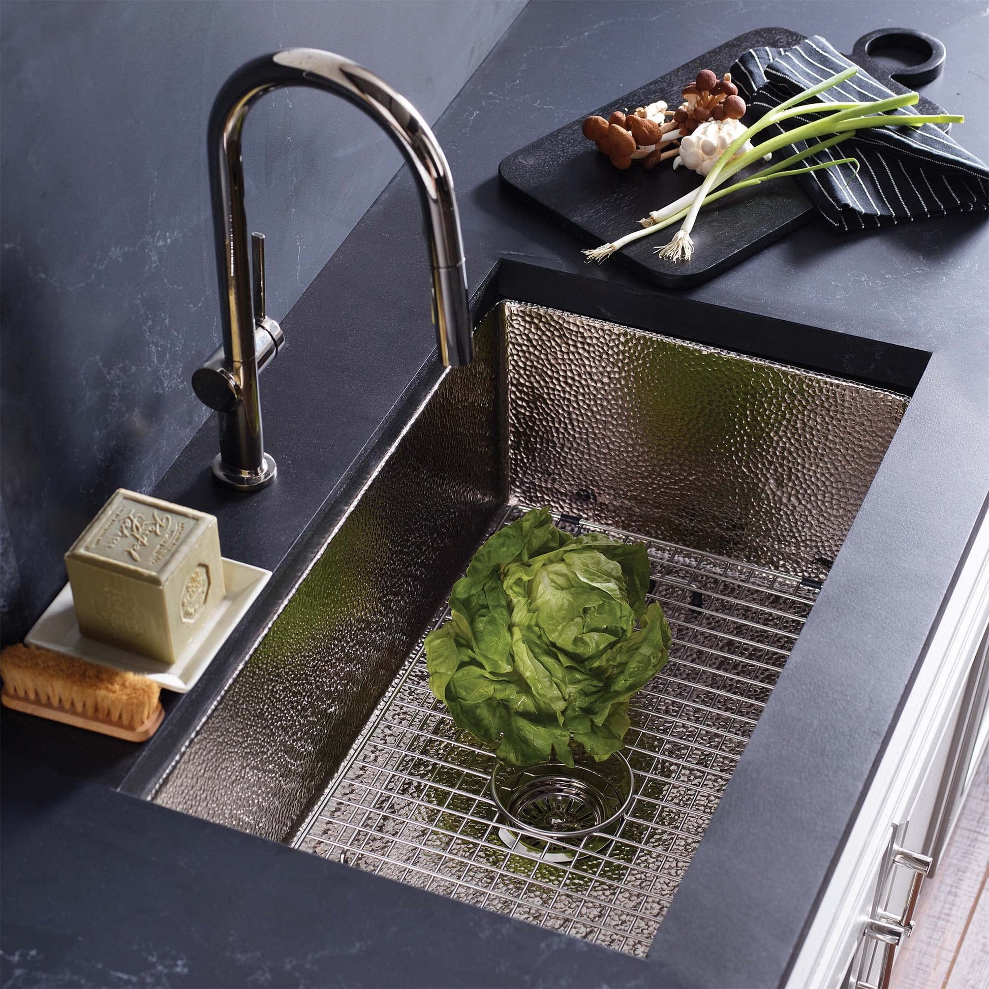 Brushed nickel undermount kitchen sink with hammered interior basin and grid insert, paired with matching faucet.