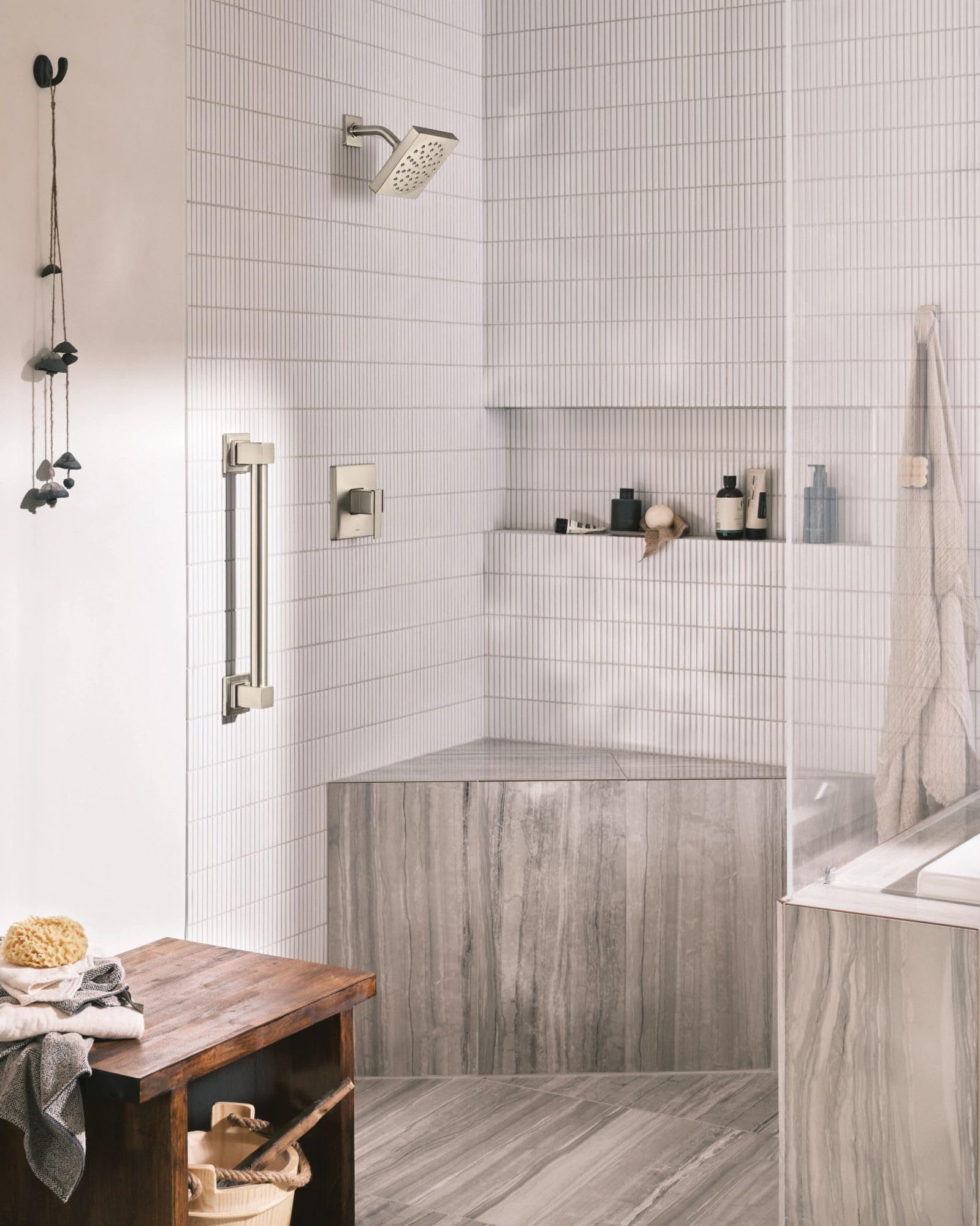 Brushed nickel shower trim kit with single handle control, showerhead, and vertical grab bar installed in tiled bathroom encl