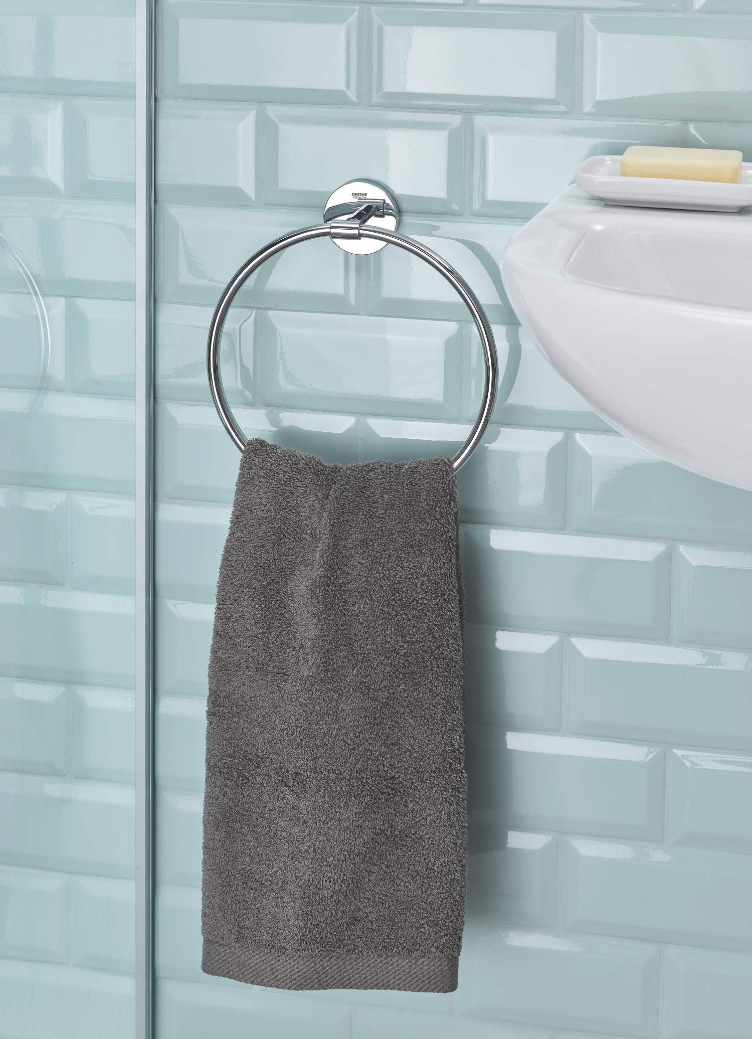 Chrome towel ring mounted on light blue tile wall with gray towel draped over circular metal ring.
