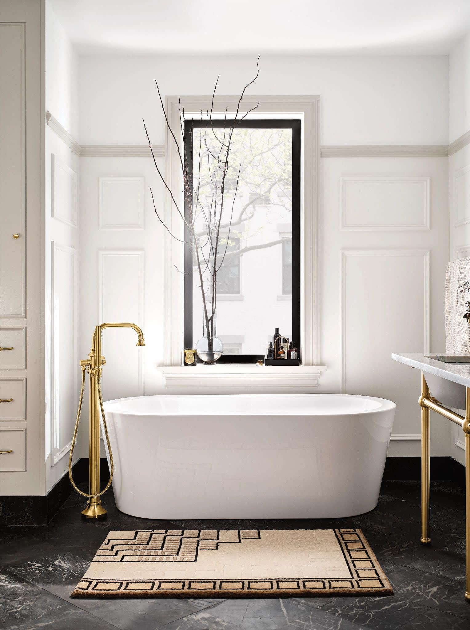 Brushed gold freestanding tub filler with single handle and curved spout next to white oval bathtub.