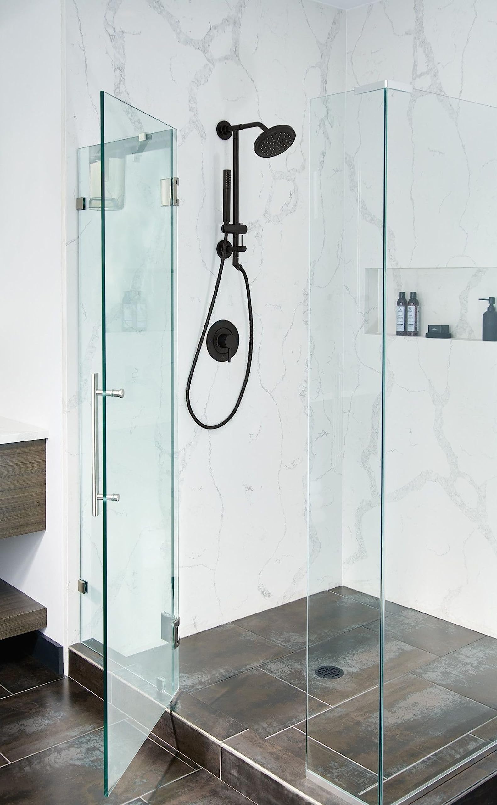 Matte black shower trim kit with lever handle, overhead rainhead, and handheld showerhead mounted on marble tile wall.