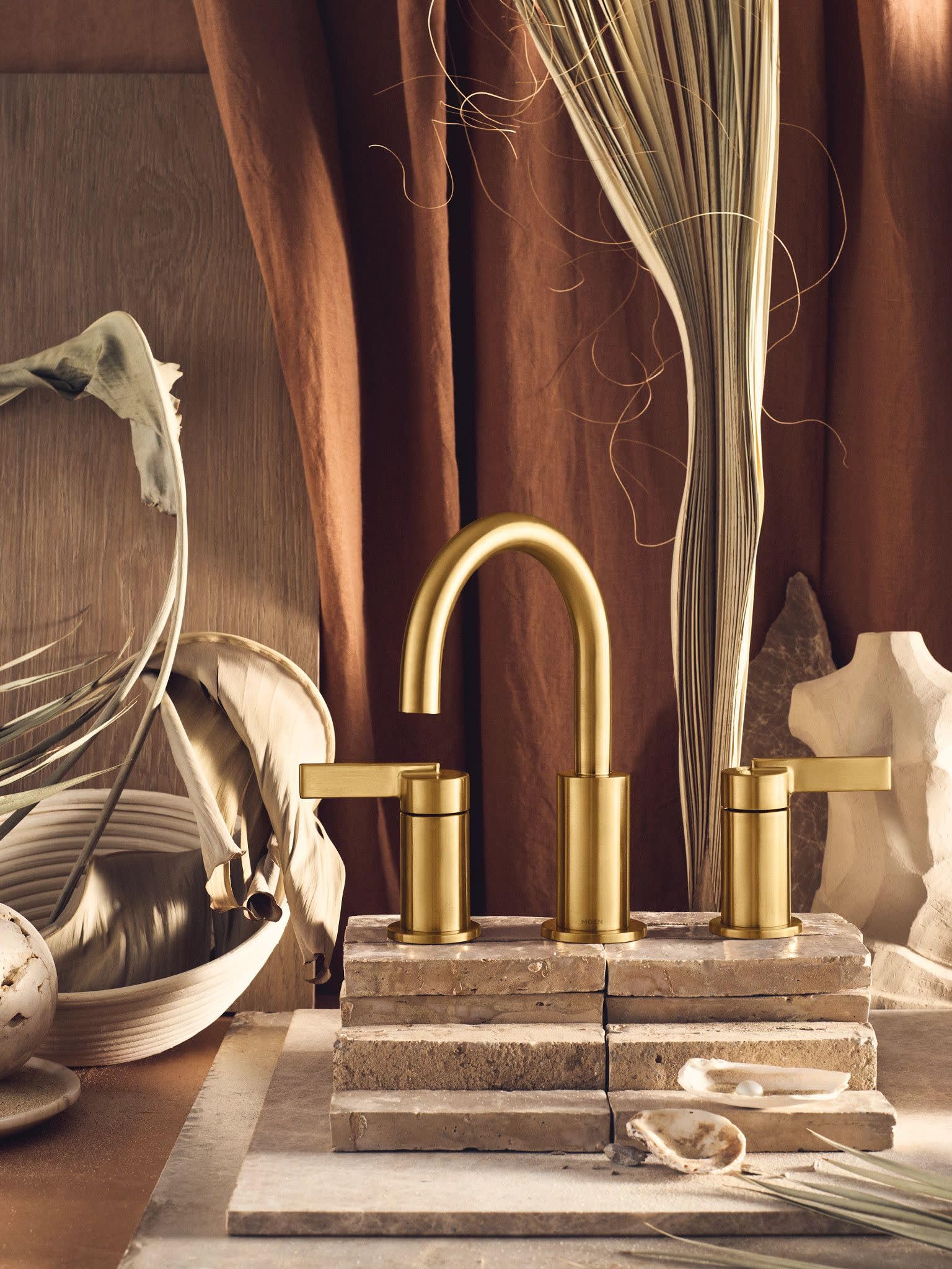 Brushed gold bathroom faucet with high arc spout and two lever handles mounted on sink deck.