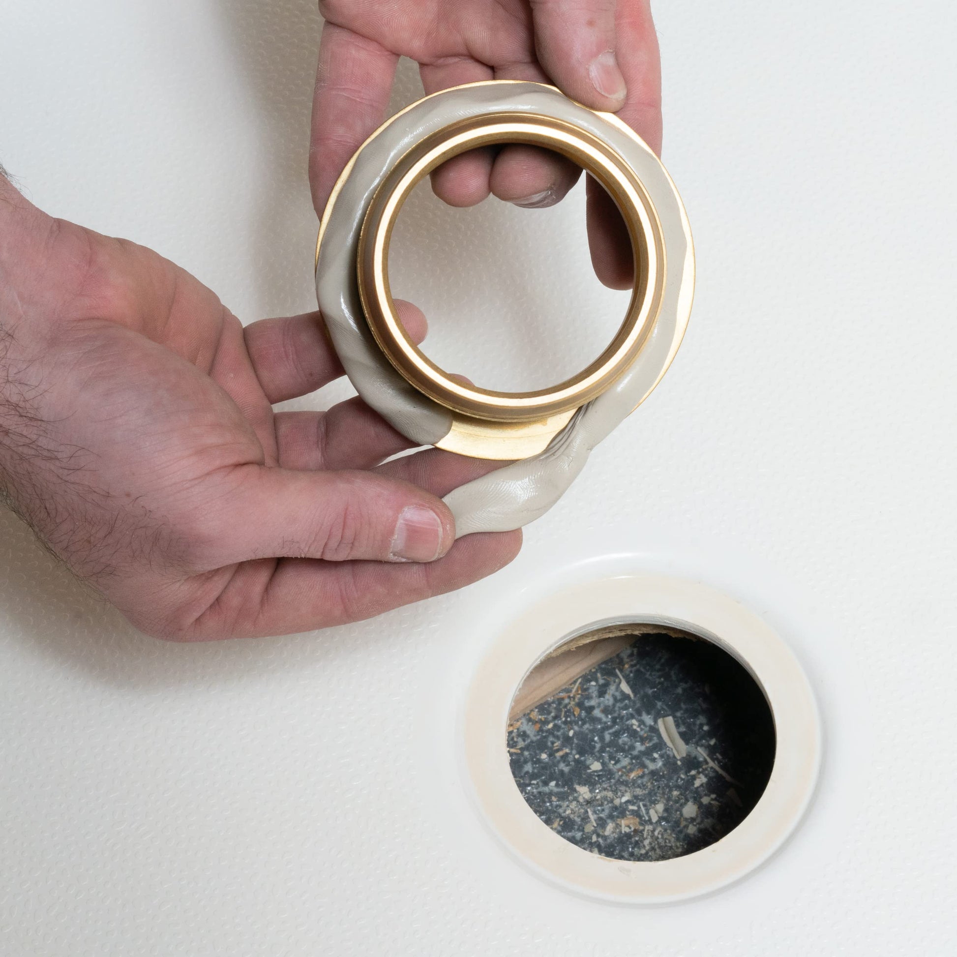Beige plumber's putty container held in hand, showing open lid with brass ring and dark sealant inside.