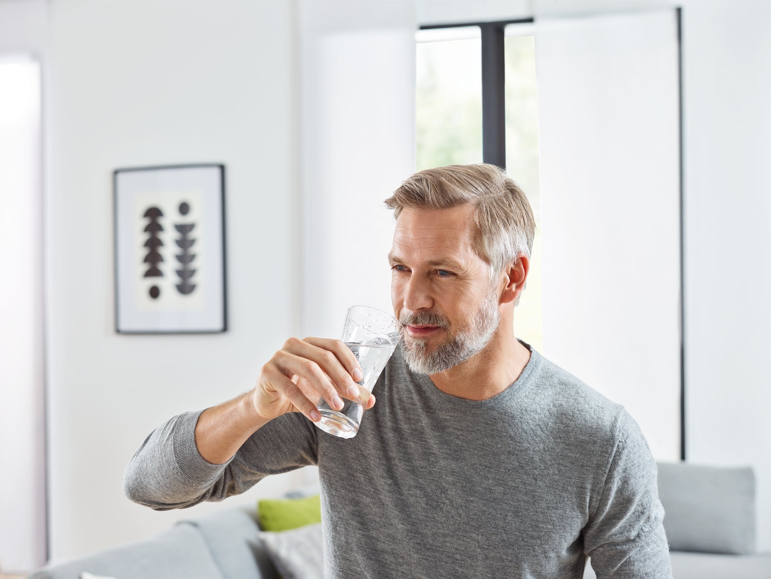 Man holding clear glass with water in modern living room interior.