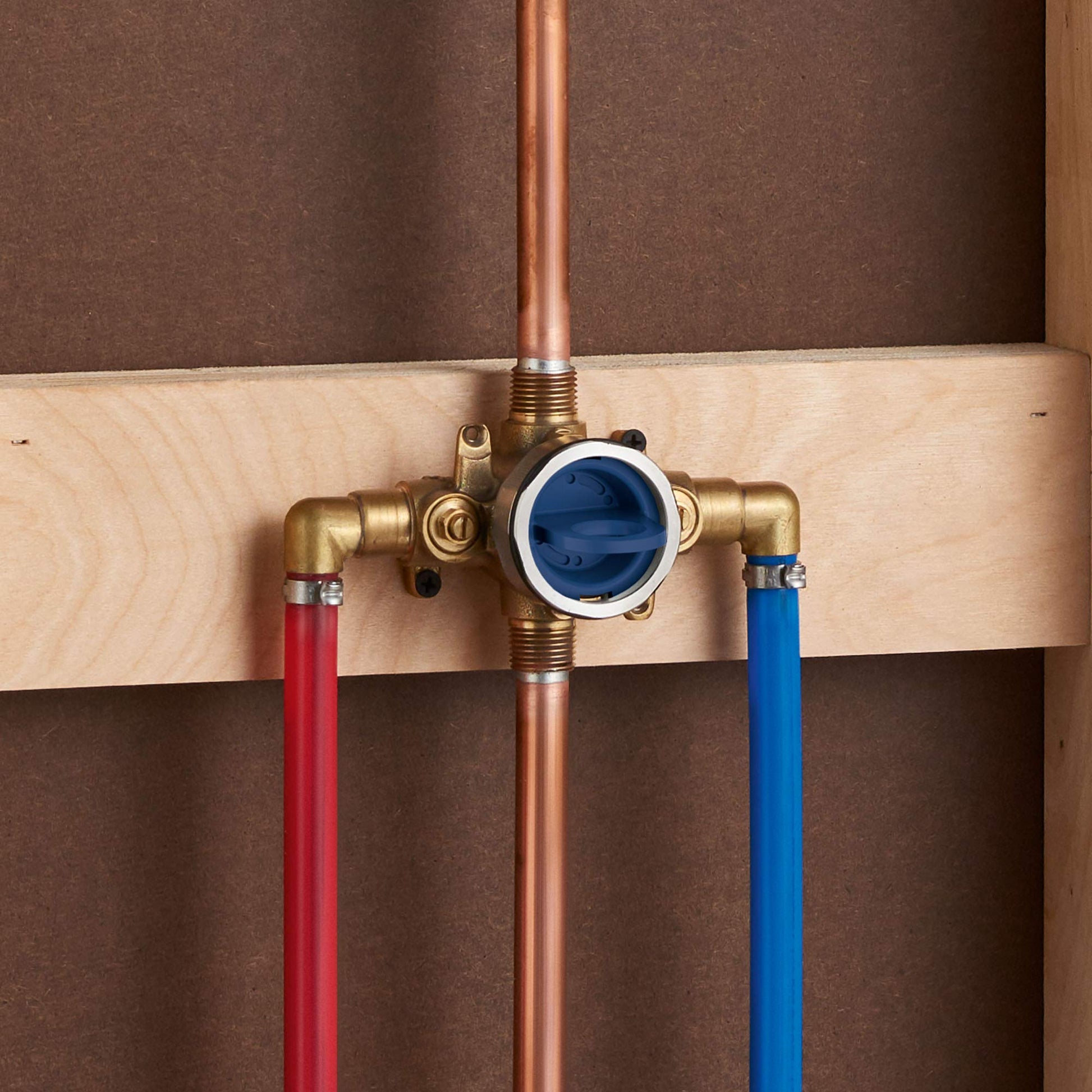 Brass pressure balance valve with white trim ring and blue cartridge center, red and blue supply lines attached to wooden bac