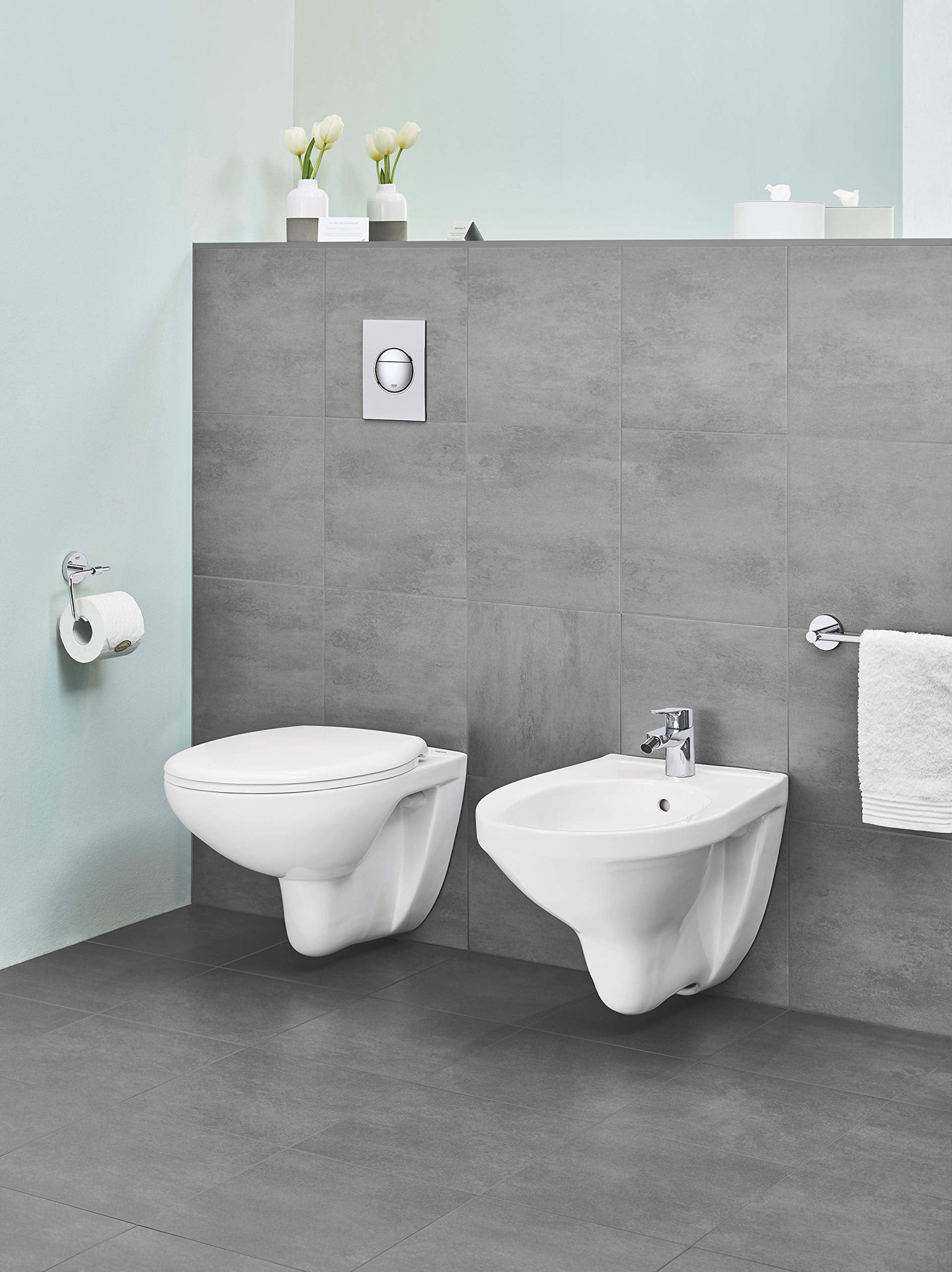 Chrome paper holder with circular ring design mounted on gray bathroom tile wall.