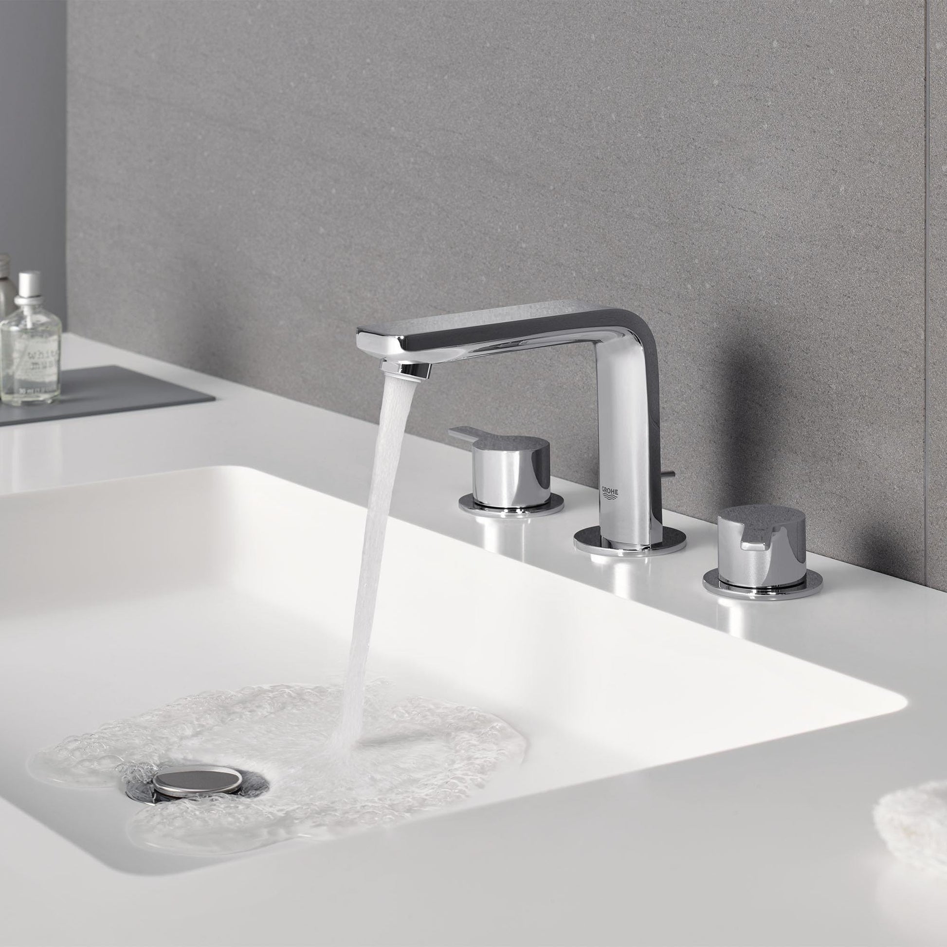 Matte black and chrome widespread bathroom faucet with curved spout and two cylindrical handles mounted on white sink basin.