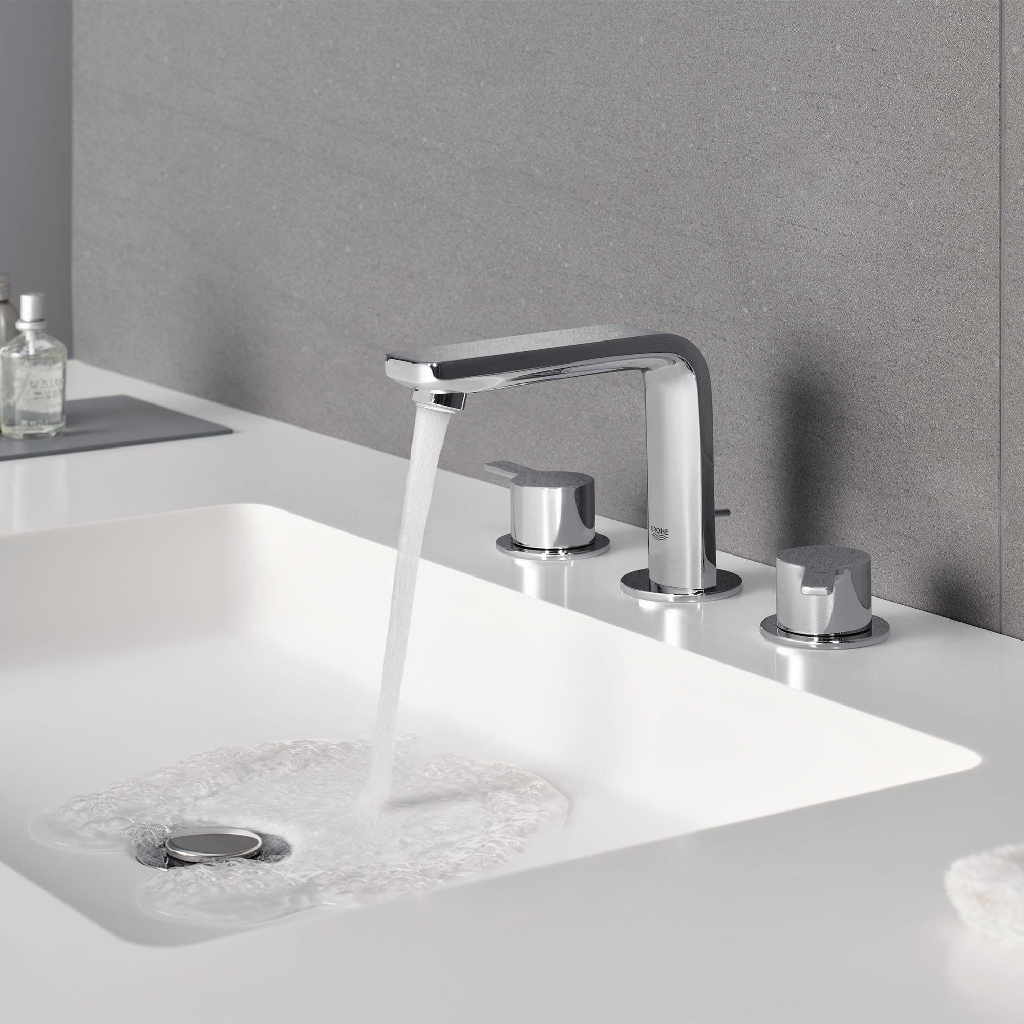 Matte black and chrome widespread bathroom faucet with curved spout and two cylindrical handles mounted on white sink basin.