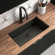 Matte black granite undermount kitchen sink with single bowl and drain, installed in wood countertop.