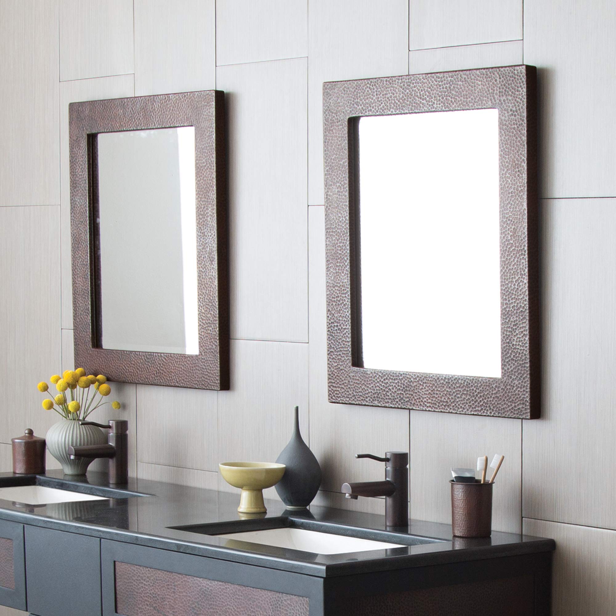 Rectangular wall mirror with textured antique copper frame mounted above bathroom vanity.