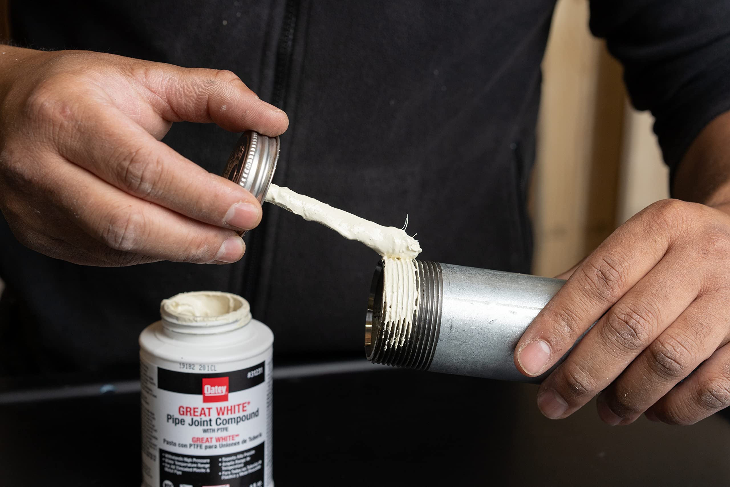 White pipe joint sealant compound being applied to threaded metal pipe fitting from 4 oz. tube.